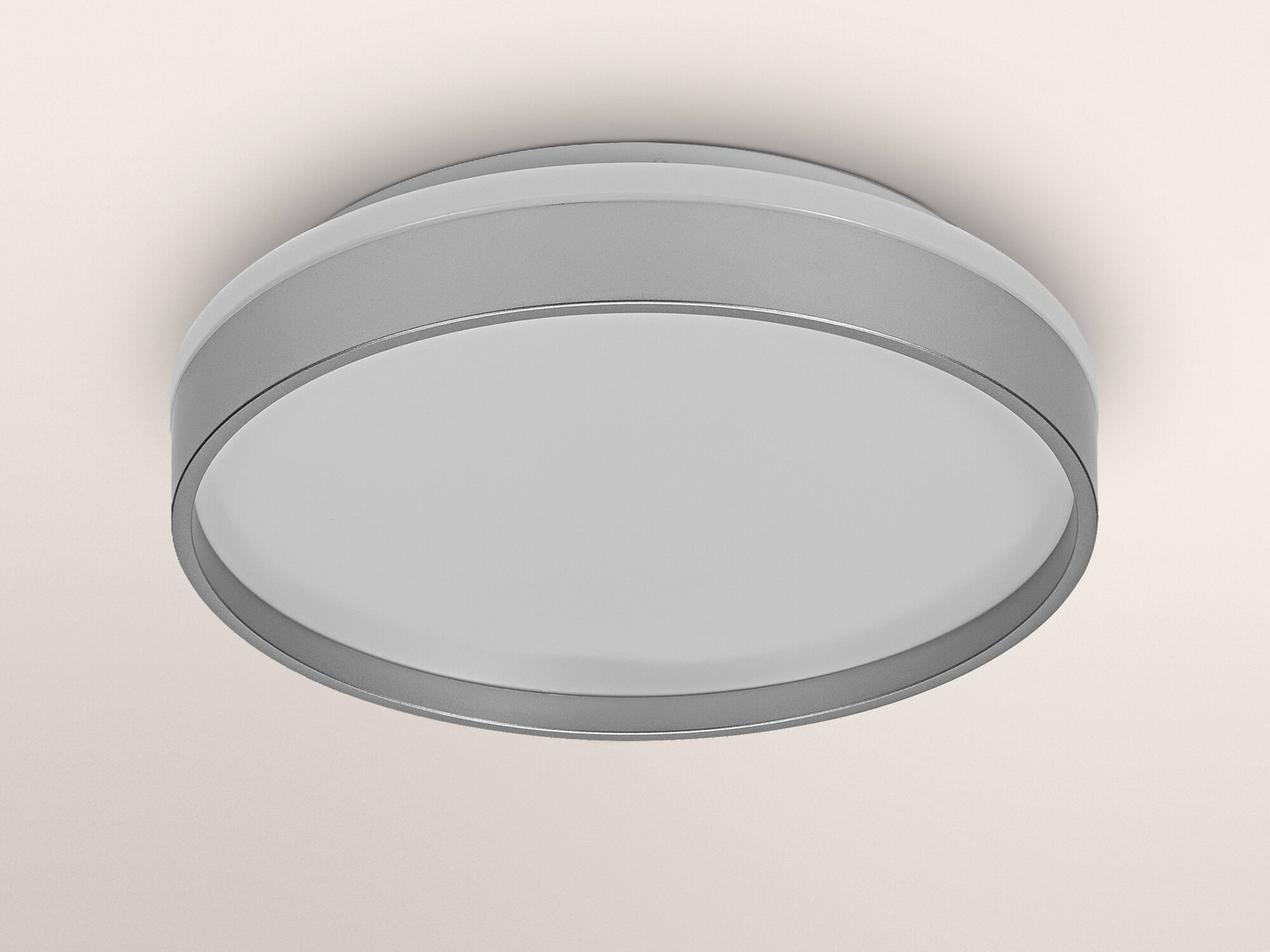 Ein kreisförmiges Deckenleuchtengehäuse mit einem weißen Diffusor und einer grauen Metallicumrandung, montiert an einer weißen Decke.