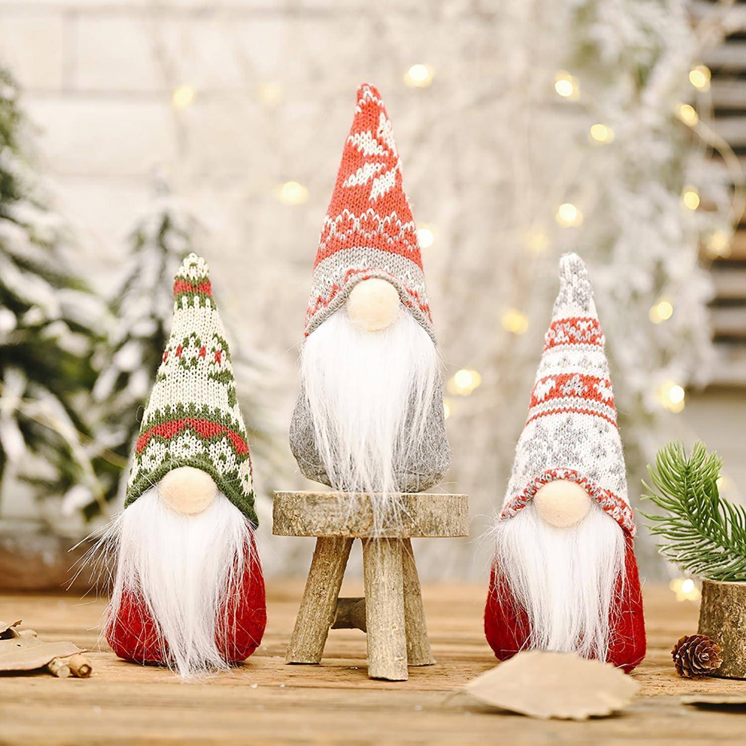 Drei festliche Gnom-Figuren mit langen weißen Bärten und spitzen Hüten in Rot, Grün und Grau sitzen auf einem Holztisch inmitten weihnachtlicher Dekoration.