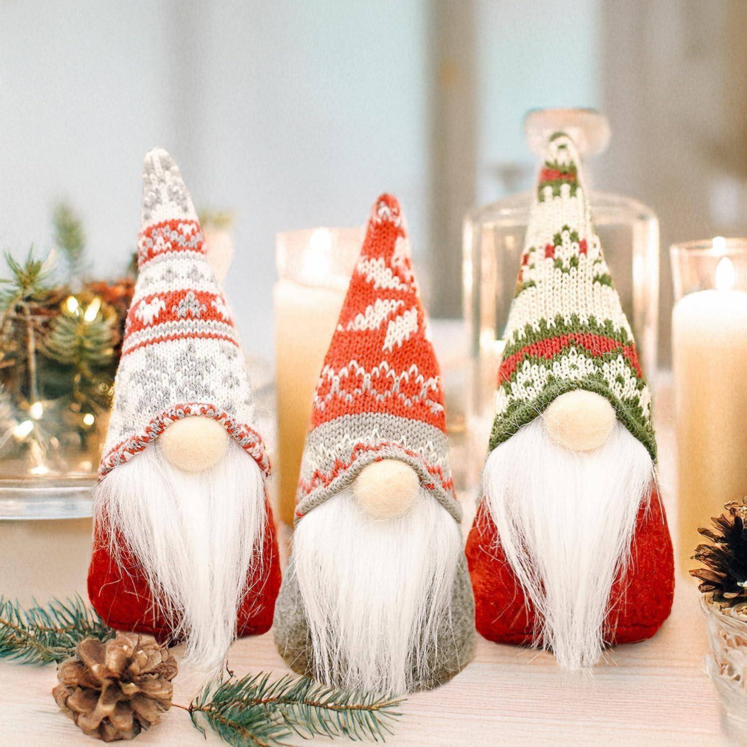 Drei festliche Gnome mit langen weißen Bärten und bunten Hüten sitzen auf einem Tisch, der mit Kerzen und Tannenzweigen geschmückt ist.