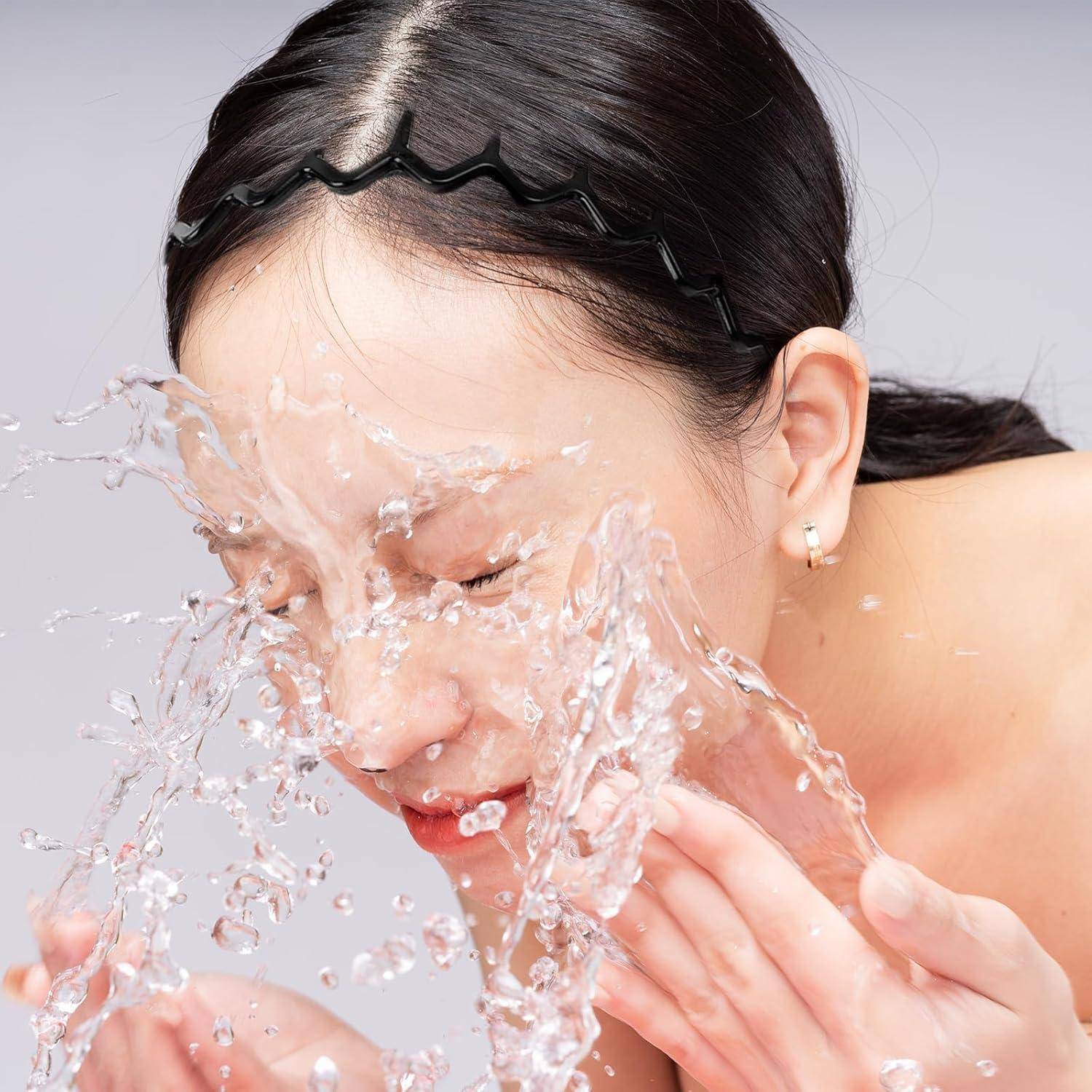 Eine Person spritzt mit beiden Händen Wasser ins Gesicht, vor einem hellen Hintergrund, was eine erfrischende Hautpfegeroutine andeutet.