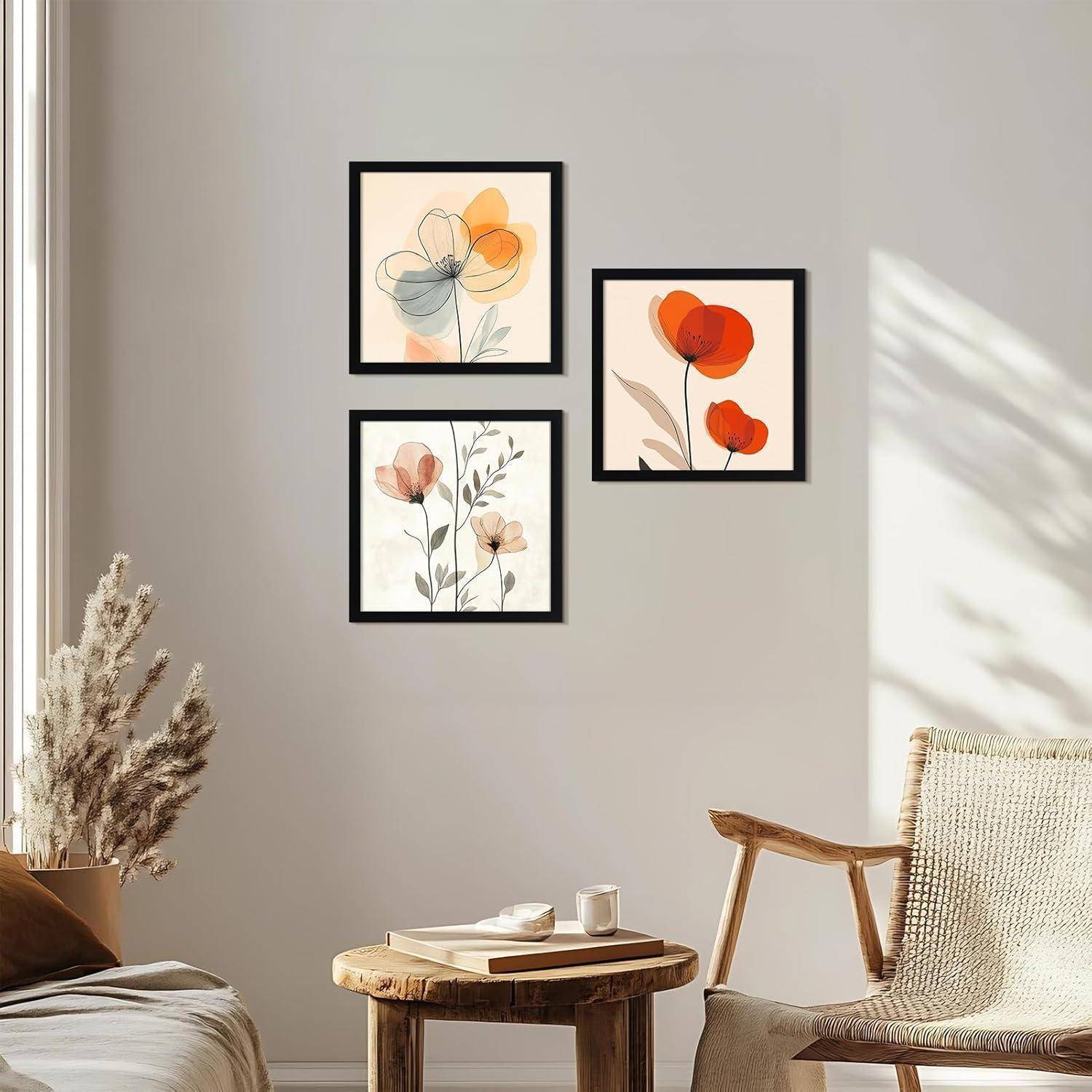 Drei abstrakte Blumengemälde in schwarzen Rahmen sind über einem Holzkaffeetisch an einer hellgrauen Wand angeordnet, mit einer kleinen Pflanze in der Nähe.