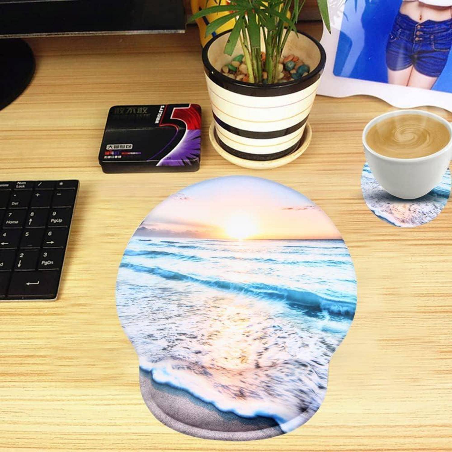Ein Schreibtisch mit einer Tastatur, einer Kaffeetasse, einem Untersetzer mit Strandszene, einer Pflanze und einem Mousepad, das einen Sonnenuntergang über dem Meer zeigt.
