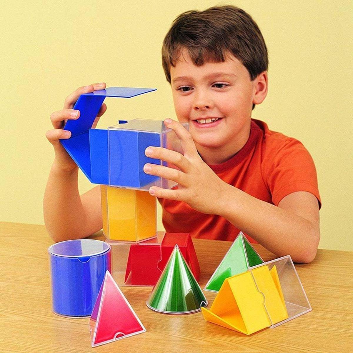 Ein Kind an einem Tisch baut mit bunten geometrischen Formen, darunter Würfel, Kegel und Pyramiden, und veranschaulicht dabei Kreativität und Lernen.