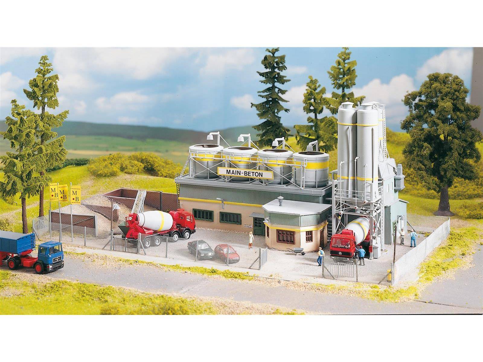 Ein Miniaturmodell einer Betonanlage mit zwei Zementfahrzeugen, Lagersilots und kleinen Fahrzeugen, eingebettet in eine ländliche Landschaft mit Bäumen.