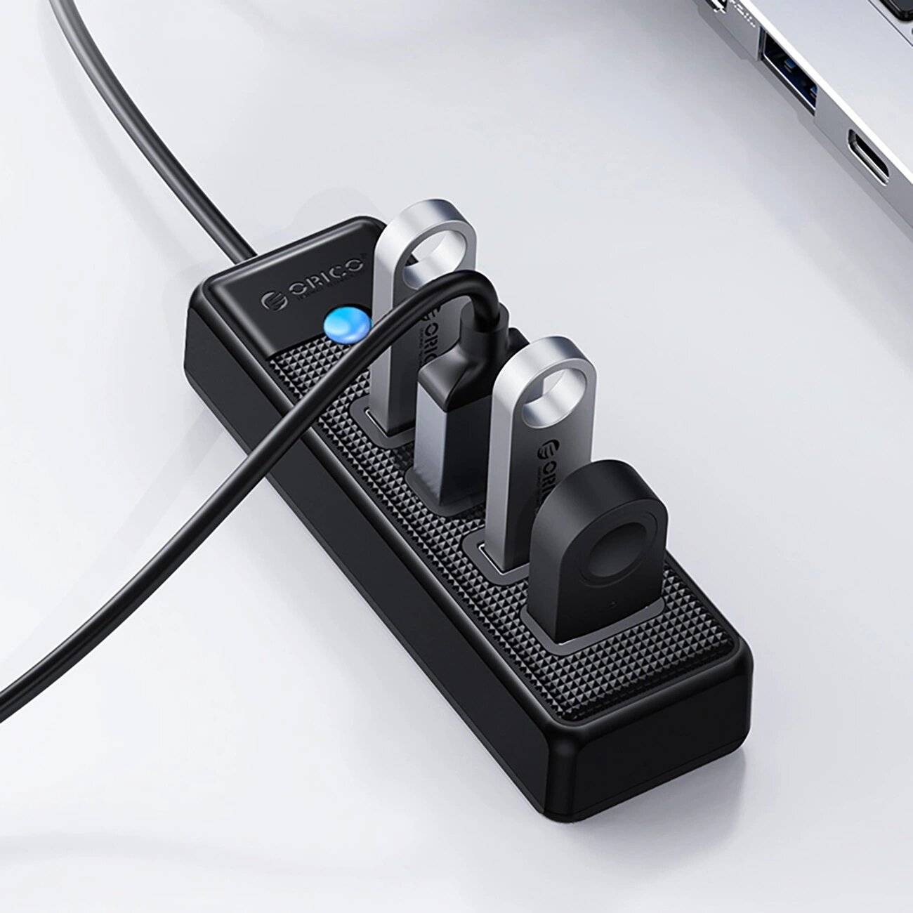 Ein USB-Hub mit drei eingesteckten USB-Laufwerken, verbunden durch ein schwarzes Kabel. Der Hub hat eine LED-Leuchte, die anzeigt, dass die Stromversorgung eingeschaltet ist.