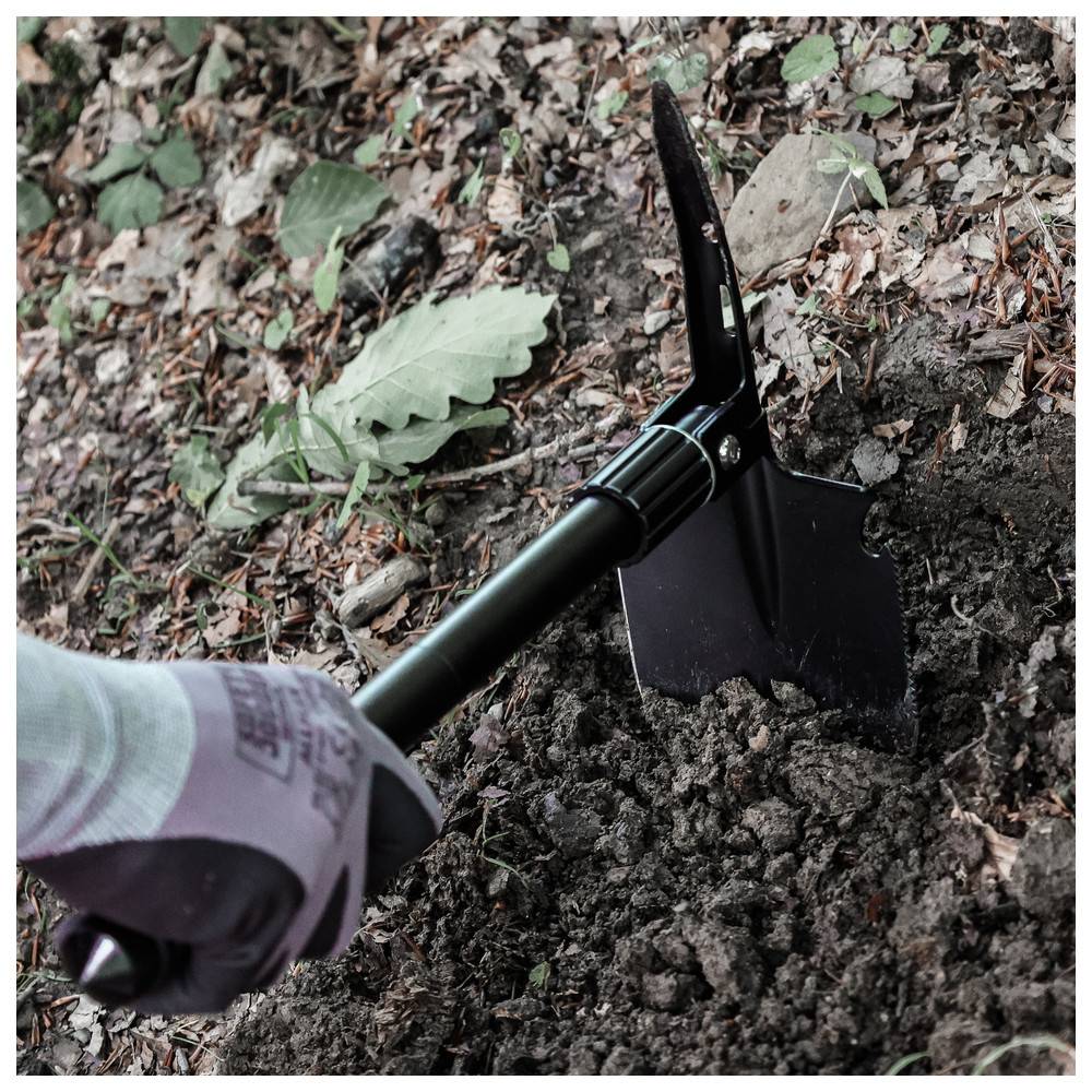 Eine Person mit Handschuhen gräbt mit einer schwarzen Schaufel in einem Garten. In der Nähe befinden sich Blätter und Reste von gedörrtem Laub.