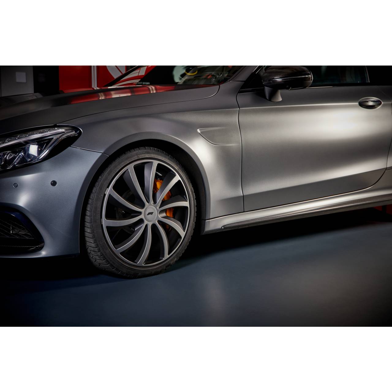 Schicker silberner Wagen aus der Nahaufnahme, Frontrad und Seitenpanel hervorgehoben, geparkt in einem dunkel beleuchteten Innenraum.