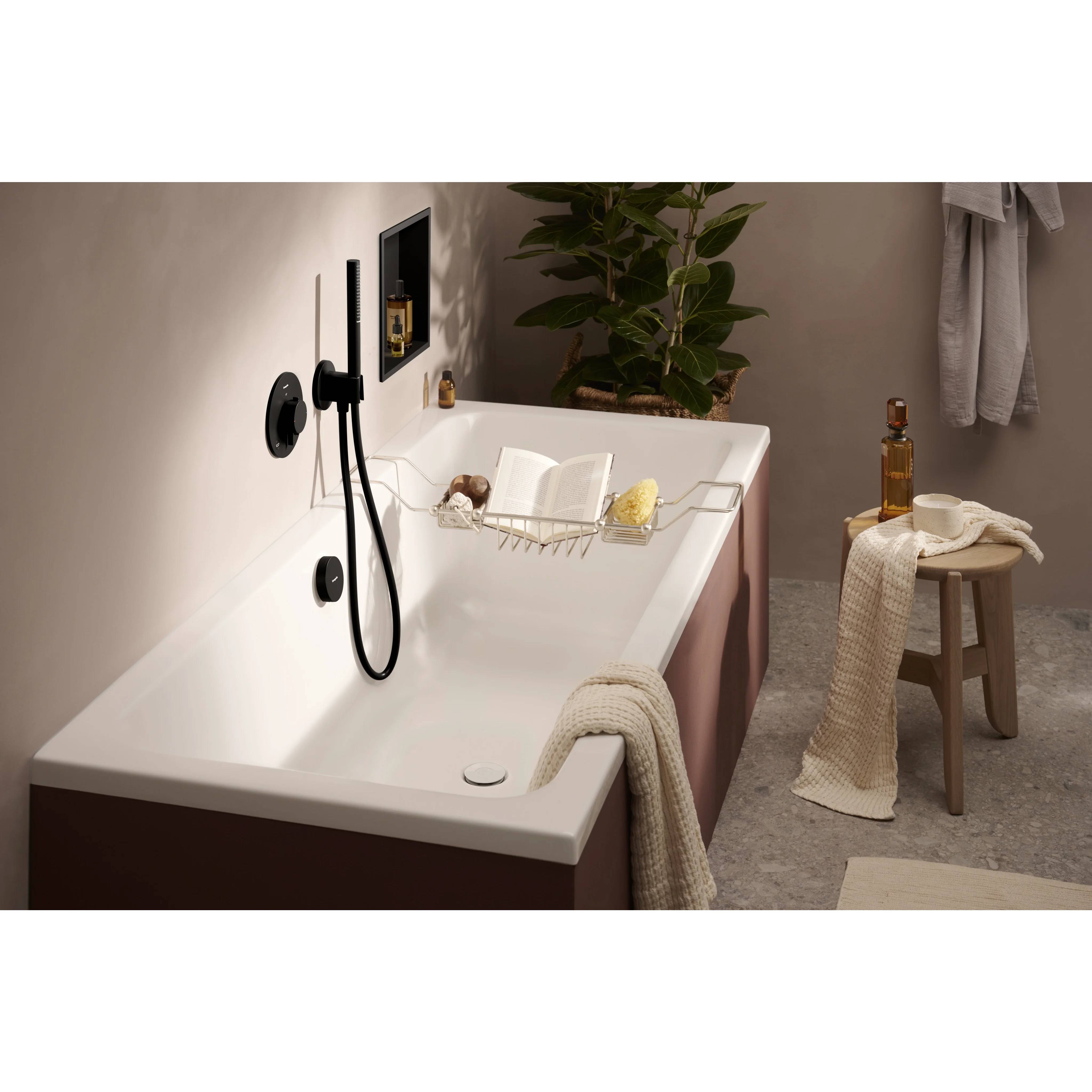 Modernes Badezimmer mit einer freistehenden Badewanne, schwarzem wandmontiertem Wasserhahn, Badewannenablage, Hocker, Handtüchern und einer Topfpflanze.