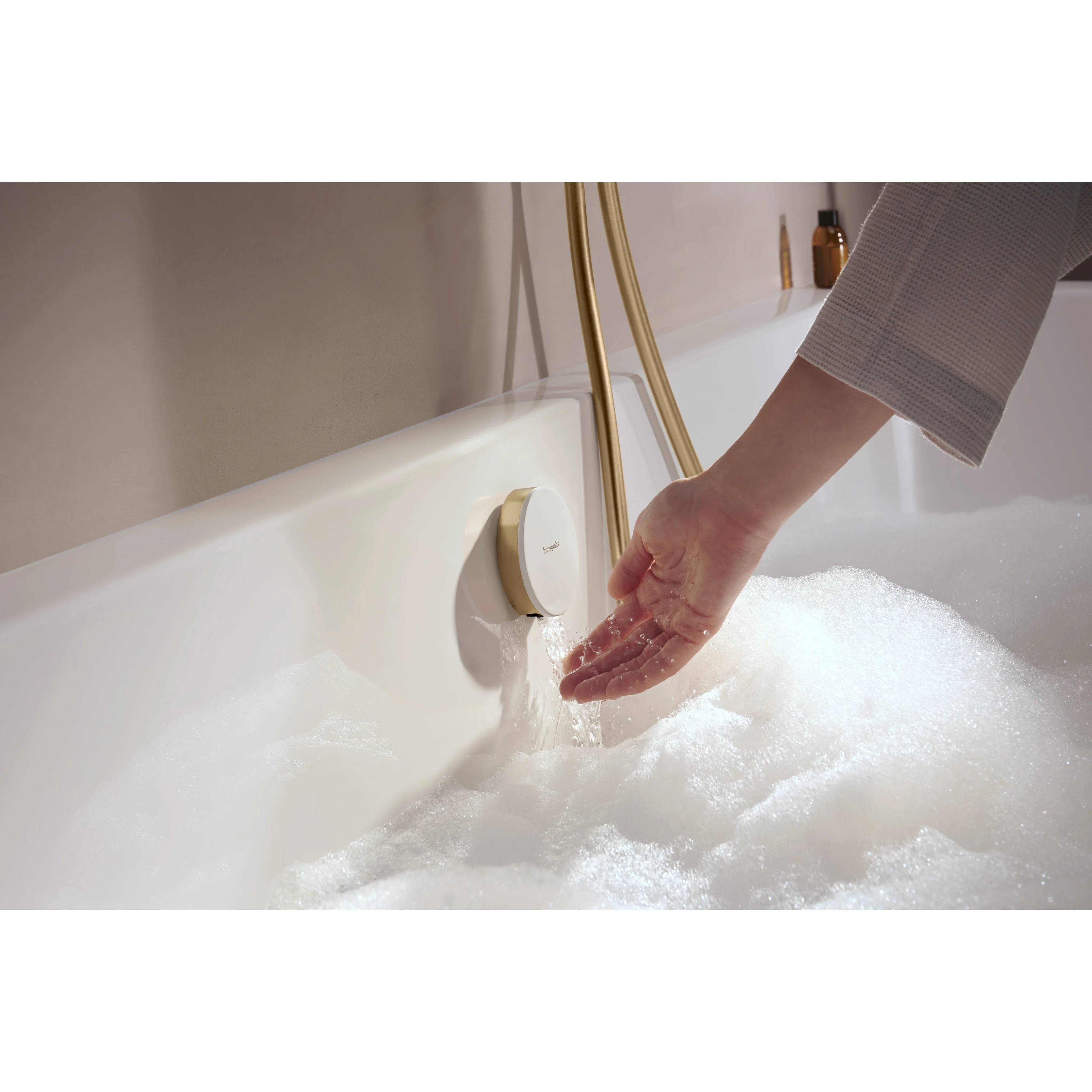 Hand testet warmes Badewasser, das aus einem goldenen Wasserhahn in eine mit Schaum gefüllte weiße Wanne fließt.