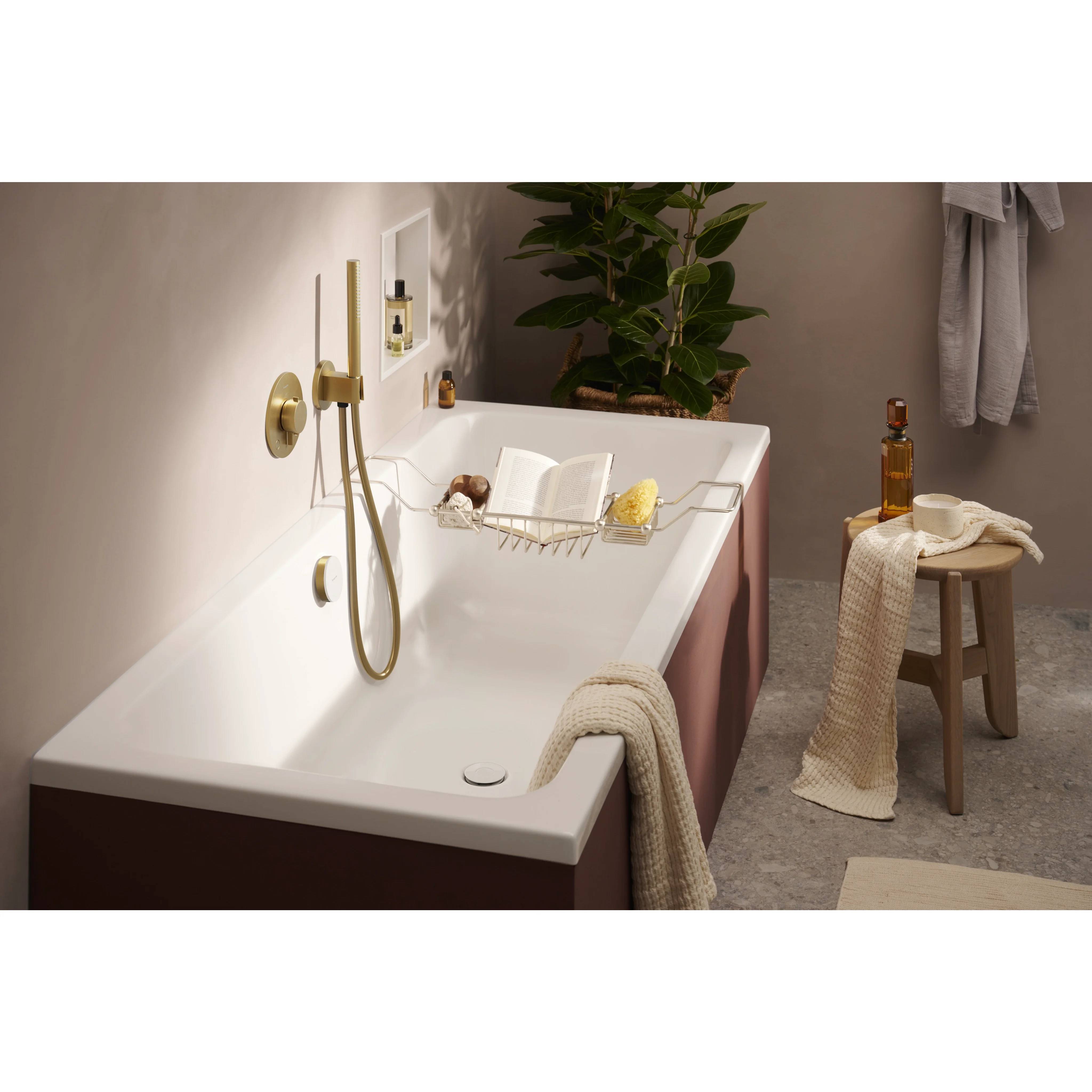 Gemütliches Badezimmer mit einer freistehenden Badewanne, Messingarmaturen, Badewannentablett, Hocker mit Flasche und Handtüchern sowie einer Pflanze in der Ecke.