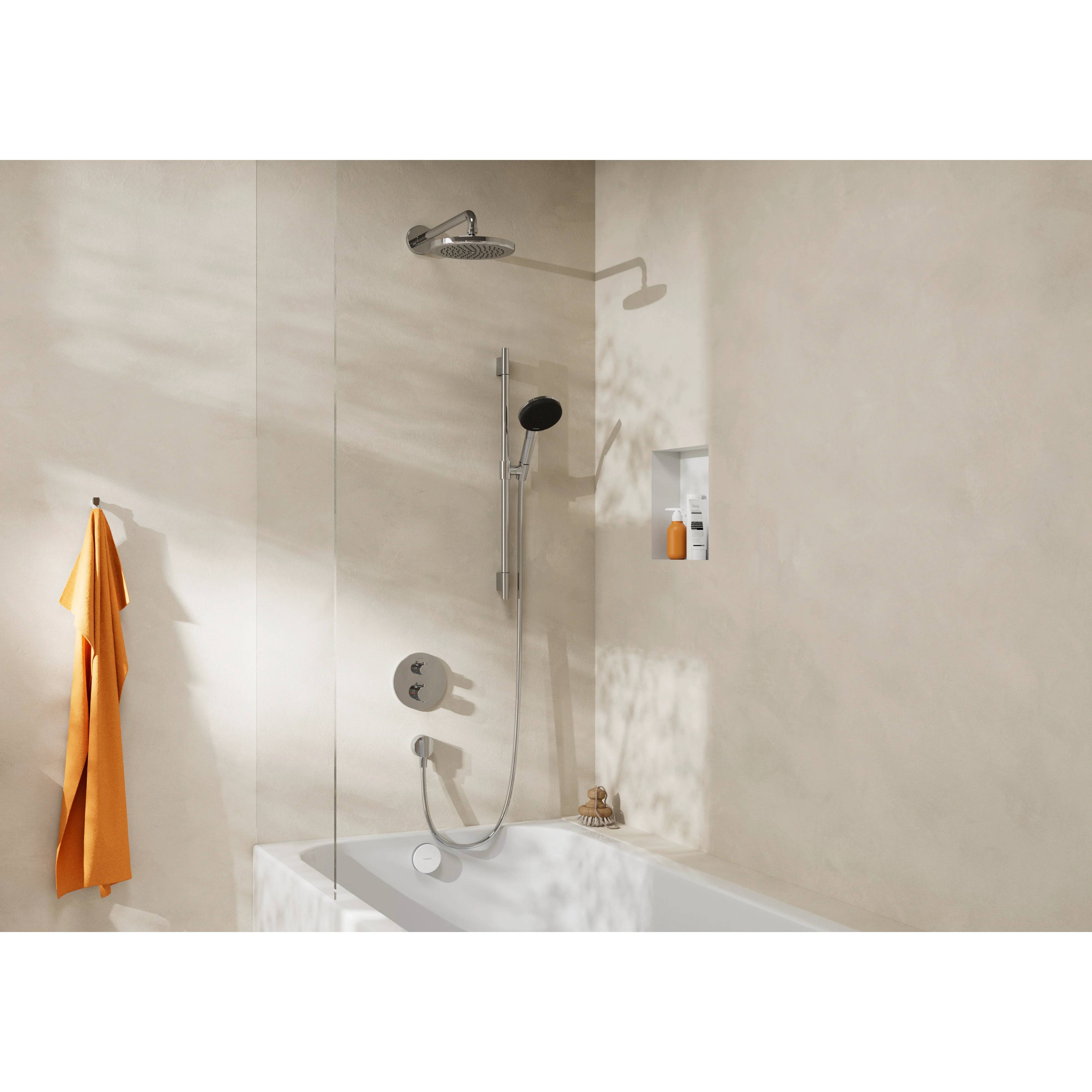 Minimales beiges Badezimmer mit einer an der Wand montierten Dusche über einer Badewanne, orangefarbenem Handtuch auf der linken Seite und einem eingelassenen Regal mit Toilettenartikeln.
