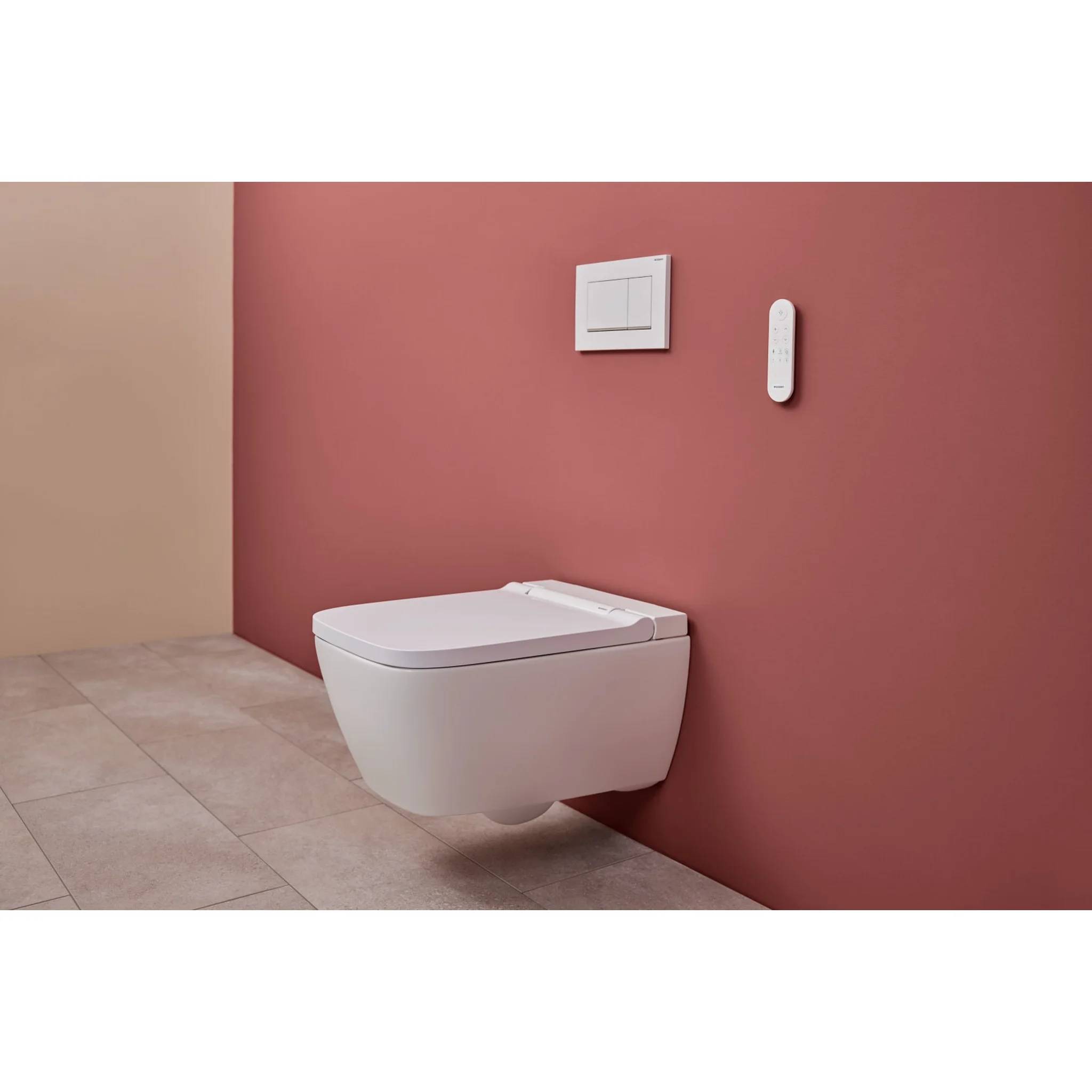 Schwebendes weiß wandhängendes Toilettenbecken an einer rosa Badezimmerwand, mit Spülplatte und Fernbedienung darüber, auf beigefarbenen Fliesenboden.