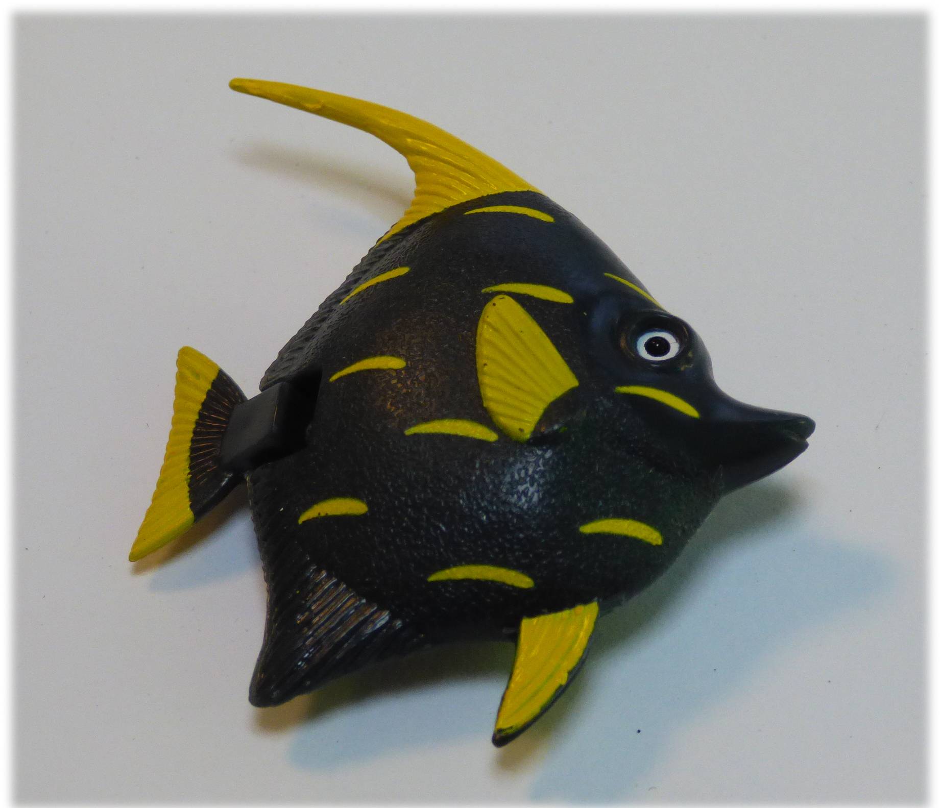 Ein Spielzeugfisch mit schwarzem Körper und leuchtend gelben Flossen und Schwanz, der auf einer weißen Oberfläche liegt.
