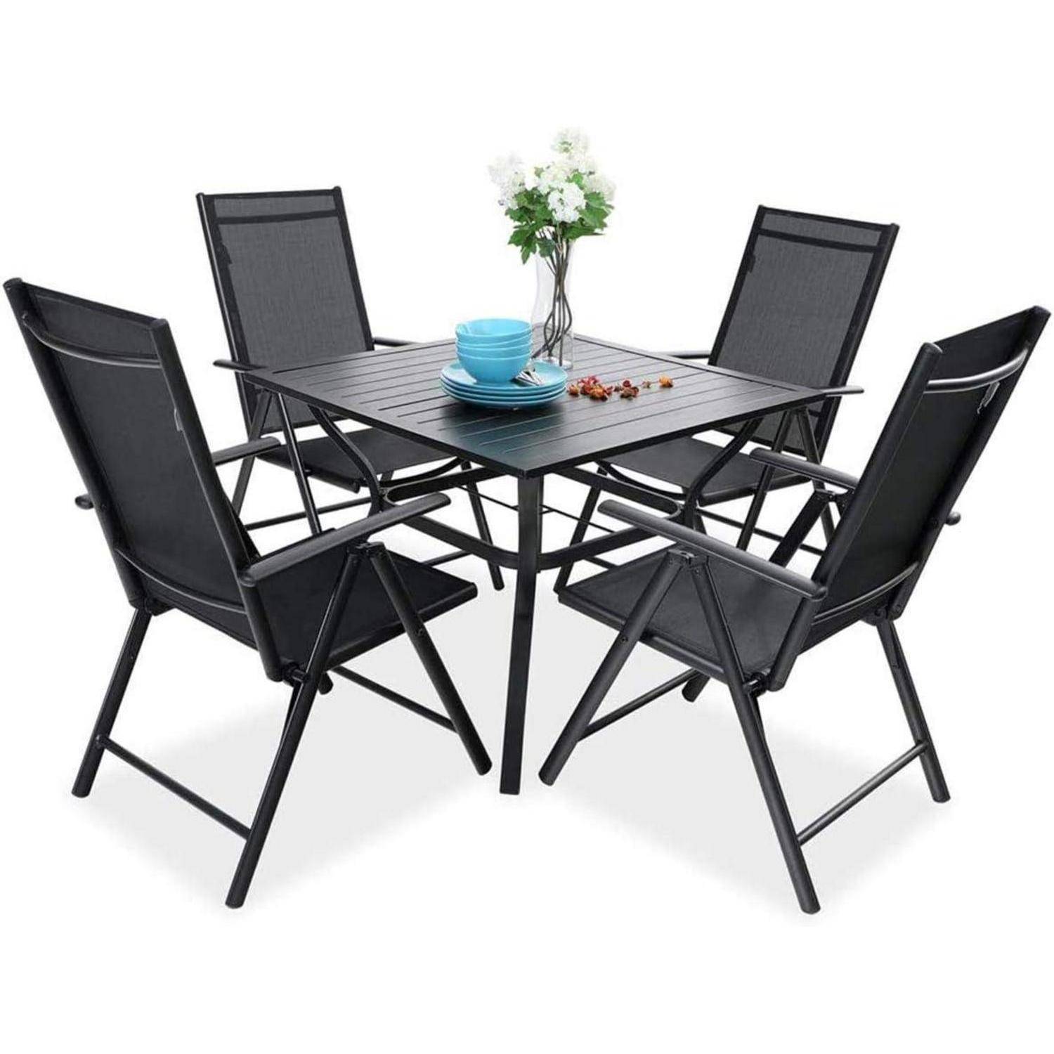 Ein schwarzes Metall-Terrassenmöbel-Set mit vier Stühlen um einen quadratischen Tisch, geschmückt mit einer Blumenvase und einem Set blauer Geschirre.