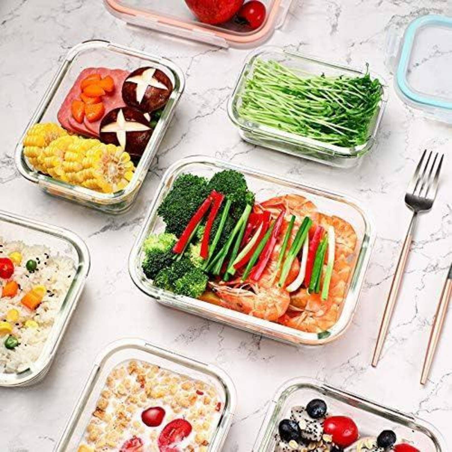 Eine Auswahl an Meal-Prep-Behältern auf einer Marmoroberfläche, wobei jeder Container mit buntem, gesundem Essen wie Gemüse, Reis und Obst gefüllt ist.