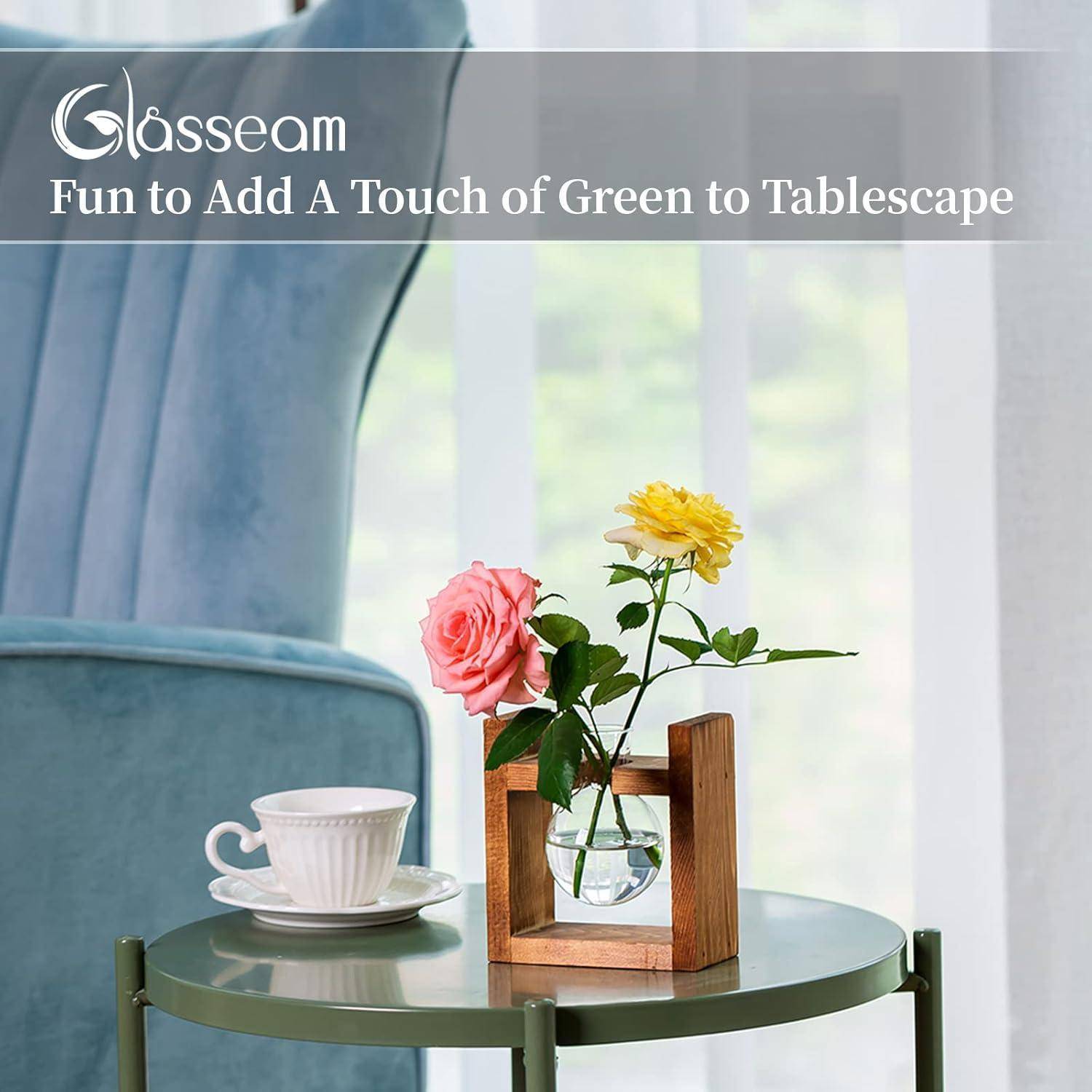 Eine kleine Vase mit rosa und gelben Blumen auf einem runden grünen Tisch neben einer weißen Teetasse. Ein blauer Stuhl befindet sich im Hintergrund.