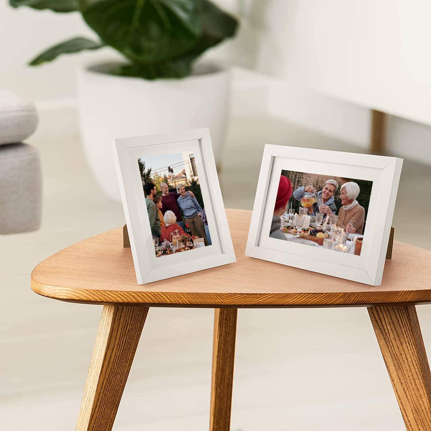 Zwei gerahmte Familienfotos auf einem Holztisch. Das linke Foto zeigt eine Gruppe im Freien, und das rechte hält Menschen beim gemeinsamen Essen fest.