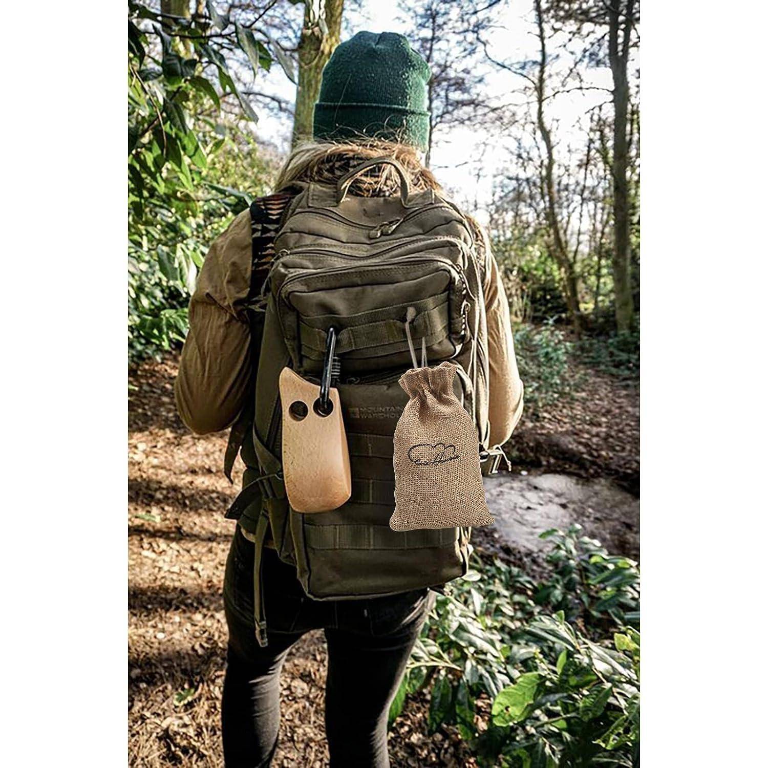 Eine Person, die Outdoor-Ausrüstung trägt, einschließlich eines grünen Rucksacks mit angebrachtem Zubehör, geht durch ein bewaldetes Gebiet im Winter.