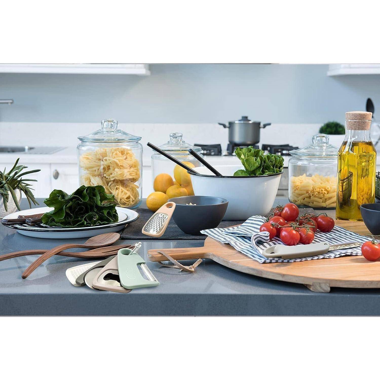 Eine moderne Küchenarbeitsplatte mit frischen Gemüsesorten, Pastaeinmachgläsern, Olivenöl und Küchenutensilien, vor einem Herd im Hintergrund.
