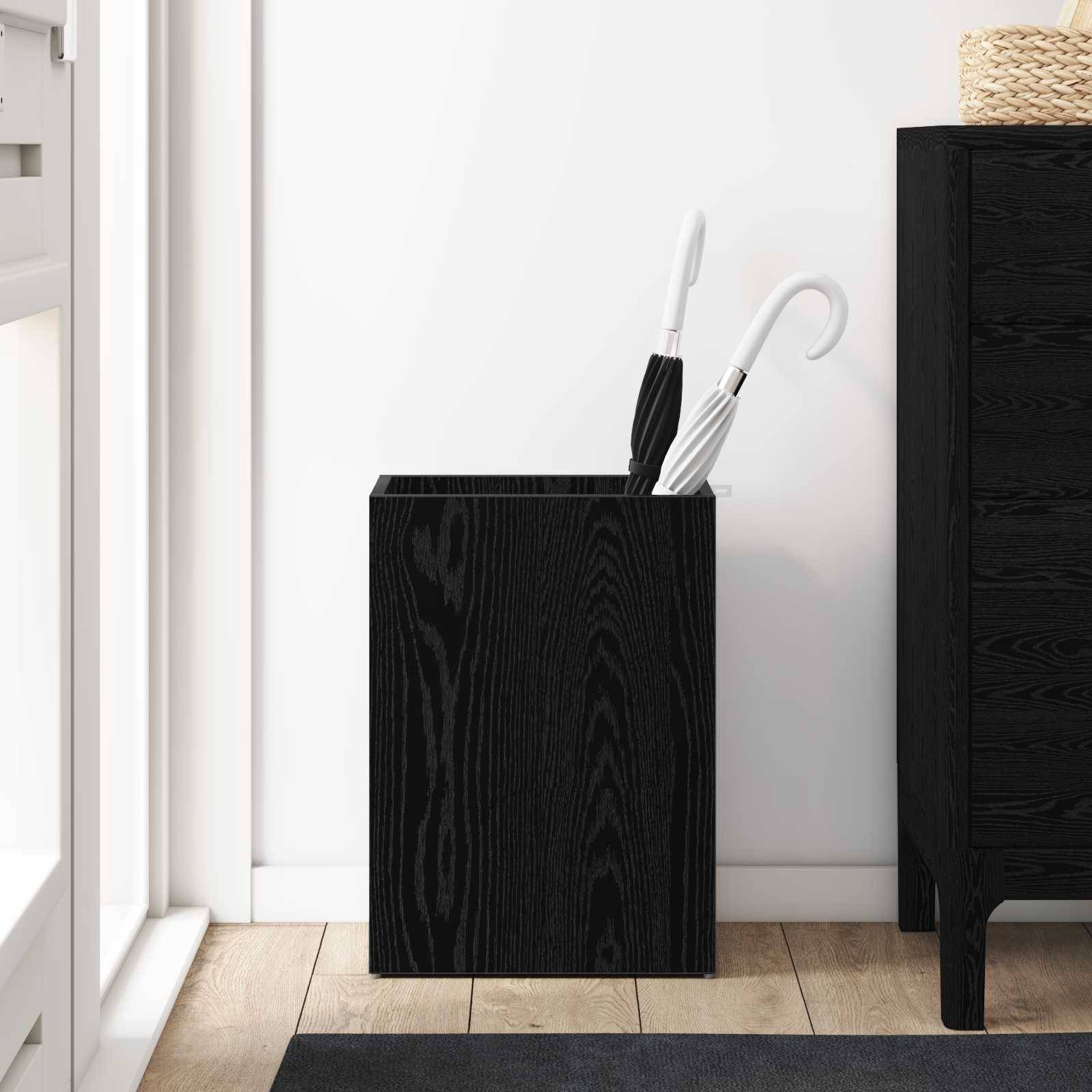 Ein schwarzer Holz-Schirmständer mit zwei weißen Schirmen steht neben einem schwarzen Holzschrank auf einem Holzboden in einem hellen Raum.
