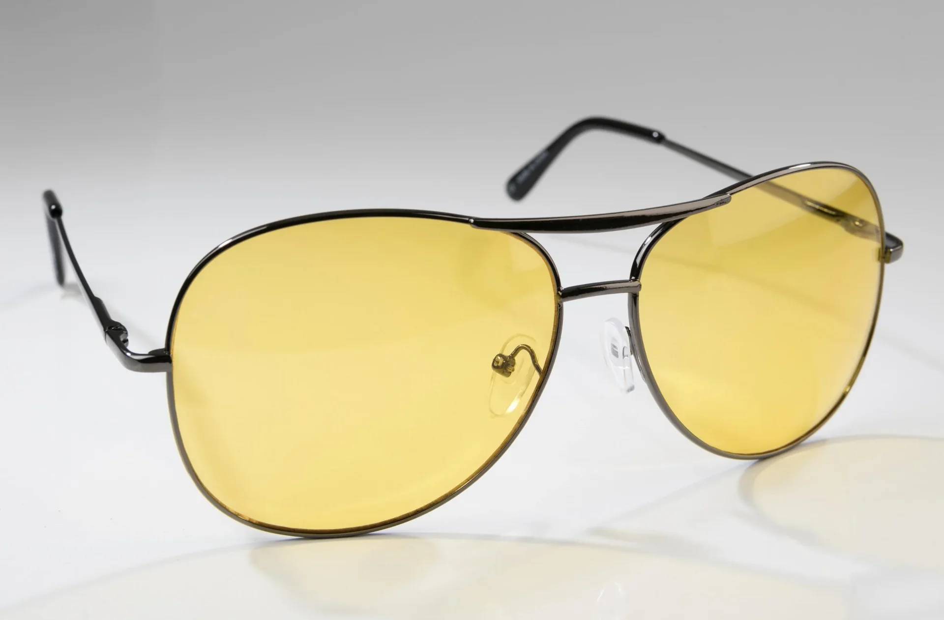 Gelb getönte Pilotensonnenbrille mit einem eleganten Metallrahmen, platziert auf einer reflektierenden weißen Oberfläche.
