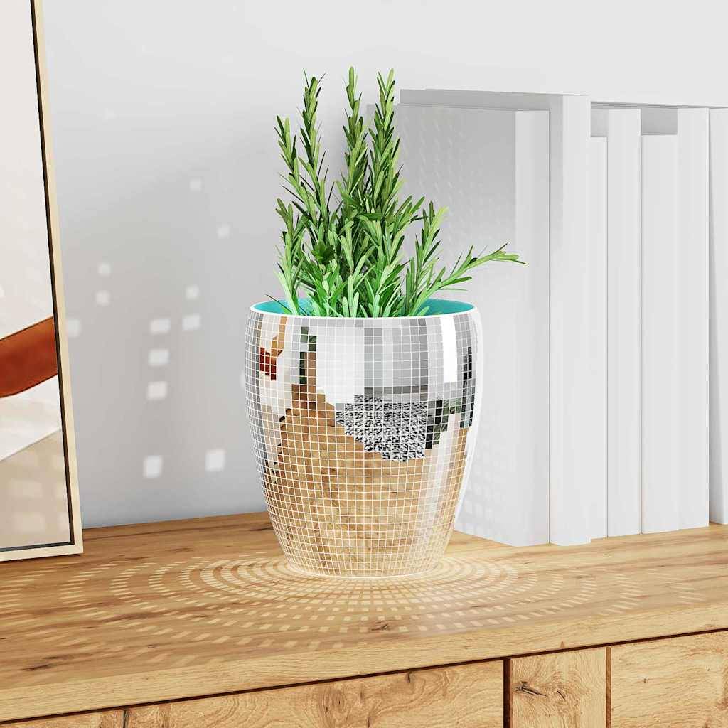 Eine dekorative Pflanze in einer reflektierenden Mosaikvase, die auf einem Holzregal neben weißen Büchern platziert ist und einen gemusterten Schatten wirft.