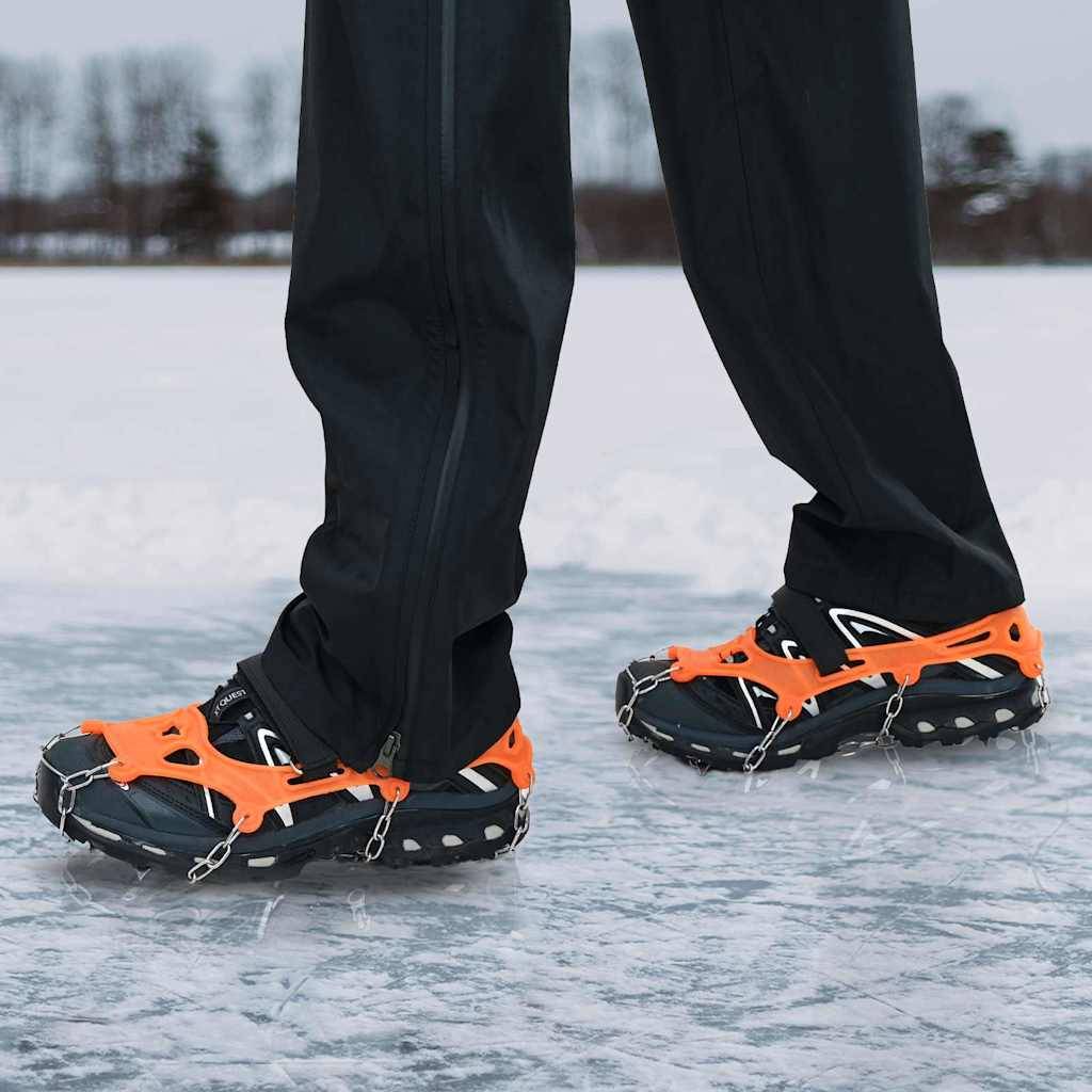 Eine Person steht auf einer verschneiten Oberfläche und trägt Hosen und Schuhe, die mit orangefarbenen Traktionsspikes ausgestattet sind, die für Eisbedingungen geeignet sind.