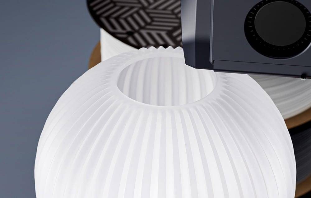 Eine Nahaufnahme eines weißen, gefälteten Lampenschirms neben einem schwarzen Lampensockel, mit einem verschwommenen gemusterten Hintergrund, der modernes Beleuchtungsdesign präsentiert.