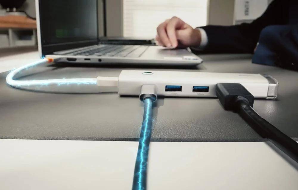 Eine Person steckt ein blitzschnell aufladbares Kabel in einen USB-Hub, der mit einem Laptop auf einem Schreibtisch verbunden ist, und veranschaulicht damit schnelle Datenübertragung oder Aufladung.