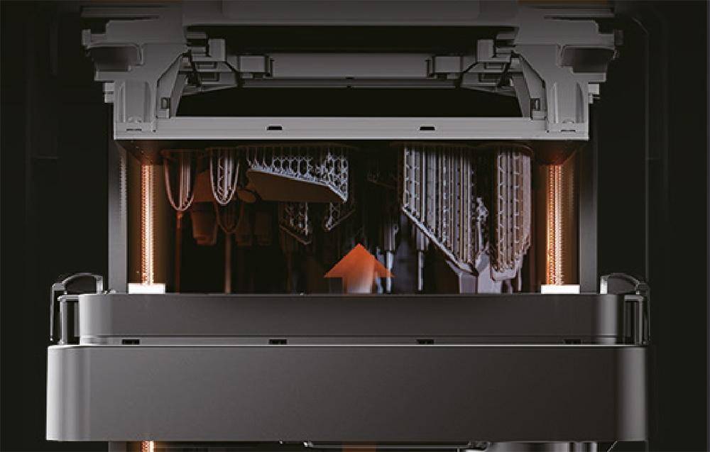 Ein 3D-Drucker bei der Arbeit, der eine komplexe, gitterartige Struktur druckt. Orangefarbenes Licht hebt die filigranen Details des entstehenden Designs hervor.