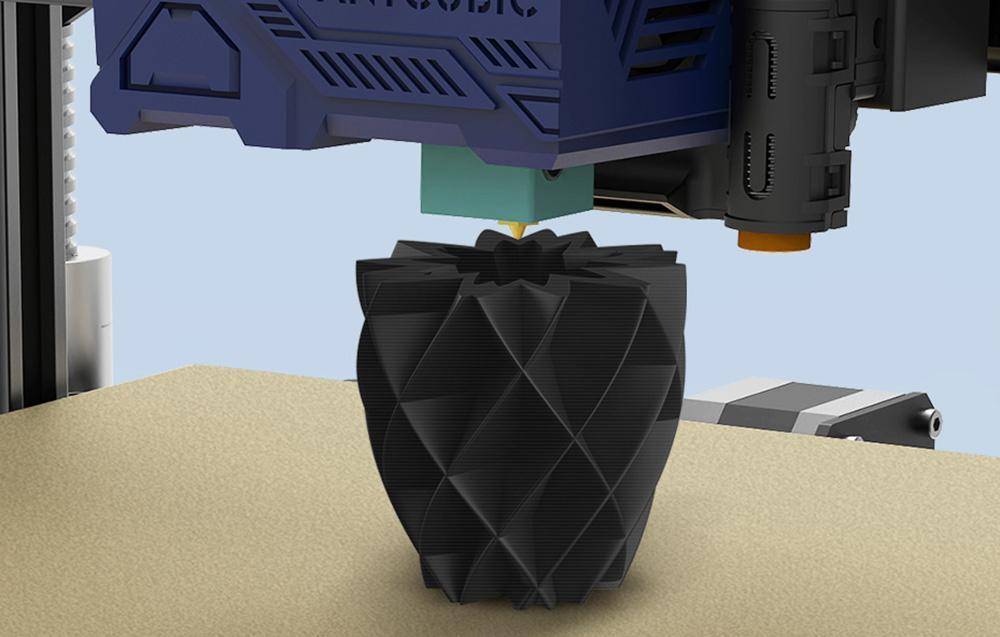 Ein 3D-Drucker erstellt ein geometrisches, schwarzes Objekt, das einer Vase ähnelt, Schicht für Schicht auf einer flachen Oberfläche.