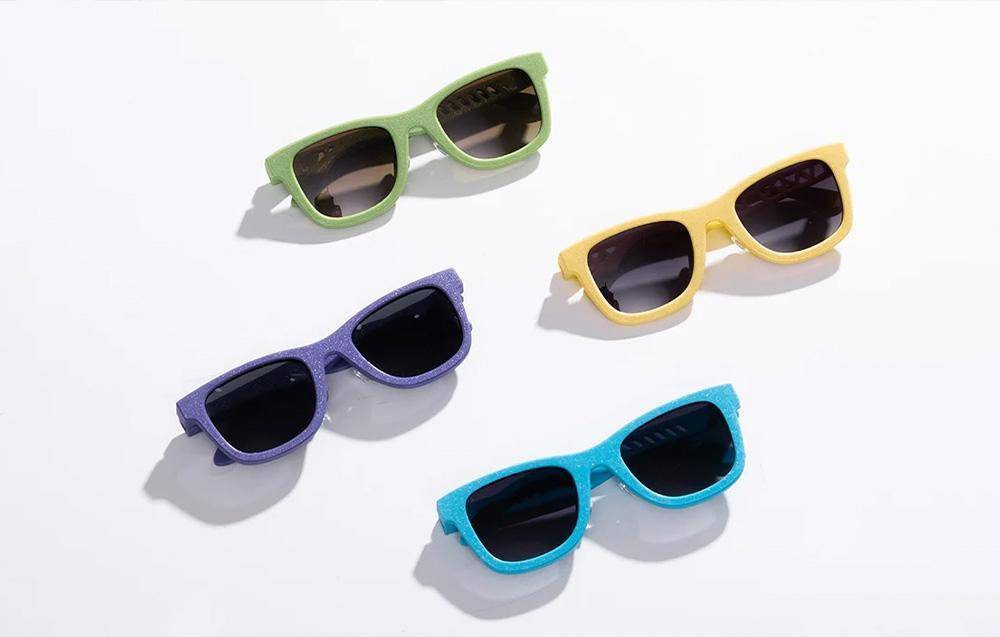 Vier Sonnenbrillen in Grün, Gelb, Lila und Blau sind auf einer weißen Oberfläche angeordnet und präsentieren verschiedene Farben und Stile.