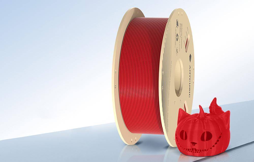 Eine Spule roten 3D-Druckfilaments mit einem kleinen roten Kürbismodell davor. Die Marke und Spezifikationen des Filaments sind auf der Spule sichtbar.