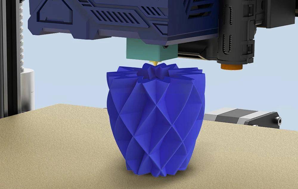 Ein 3D-Drucker, der eine blaue geometrische Vase erstellt, wobei komplexe Muster sichtbar sind, während die Düse sich über dem teilweise fertigen Objekt bewegt.