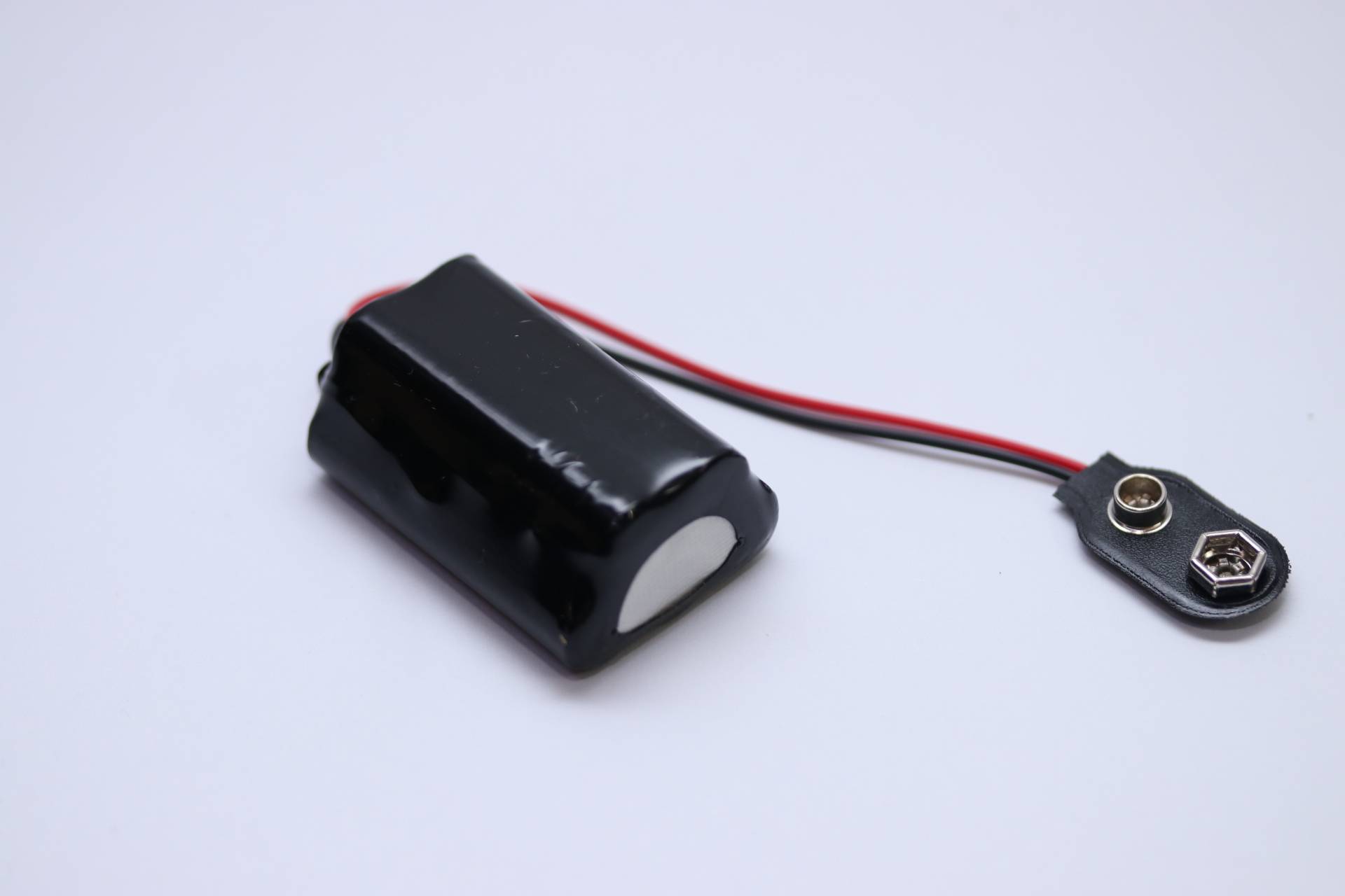 Ein schwarzer Akkupack mit roten und schwarzen Kabeln, der auf einem weißen Hintergrund liegt.