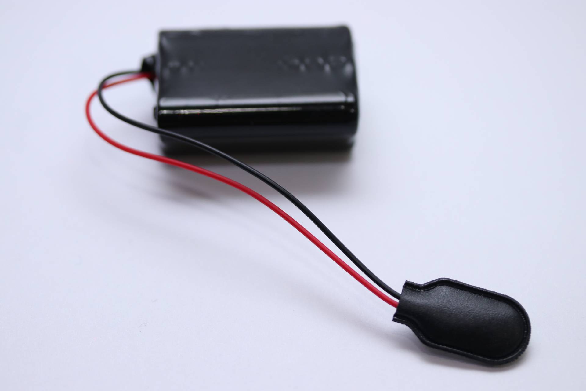 Eine kleine schwarze rechteckige Batterie mit roten und schwarzen Kabeln, die von einem Ende abstehen, auf einer weißen Oberfläche platziert.