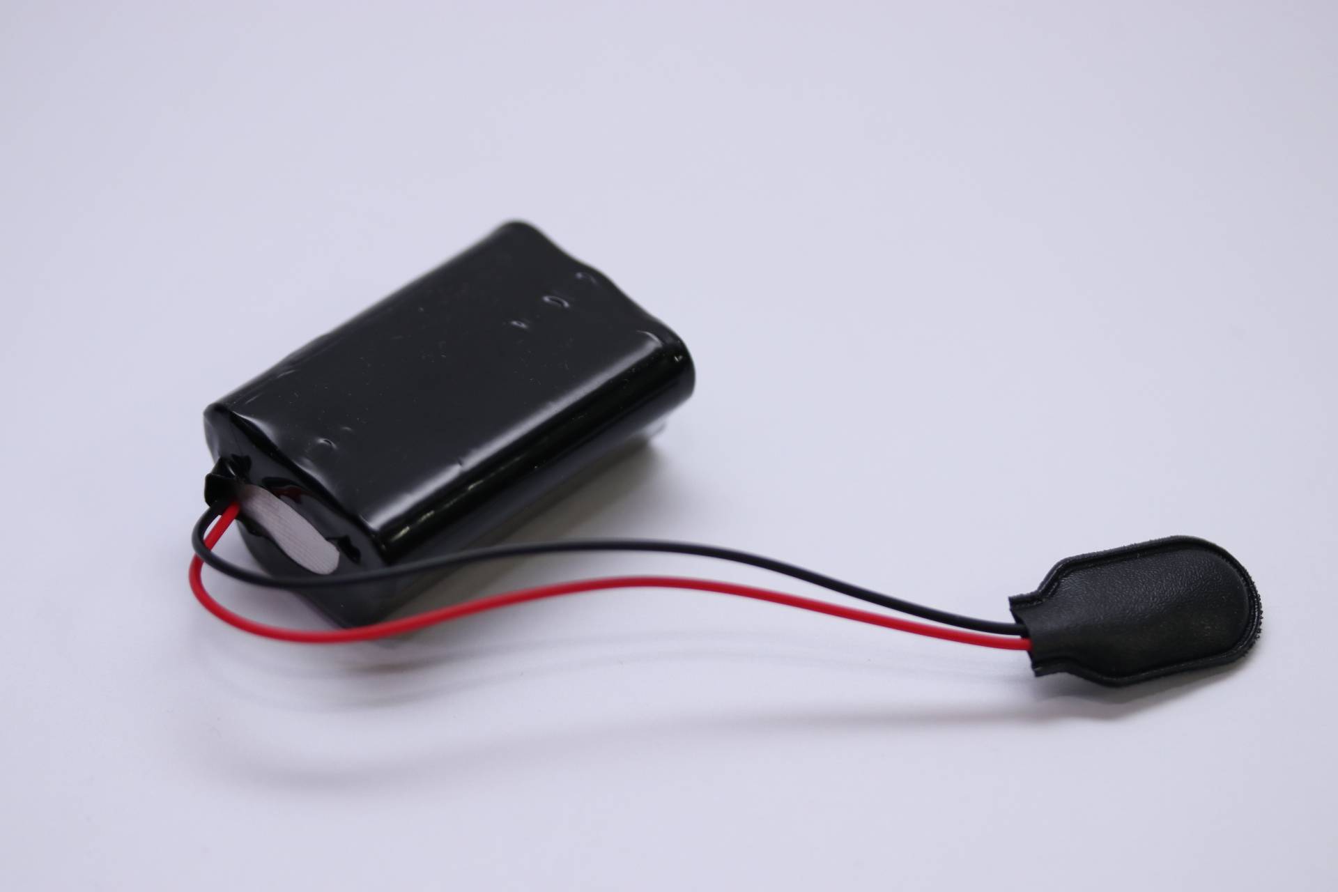 Eine kleine schwarze rechteckige Batteriebox mit roten und schwarzen Kabeln, auf einer weißen Oberfläche platziert.