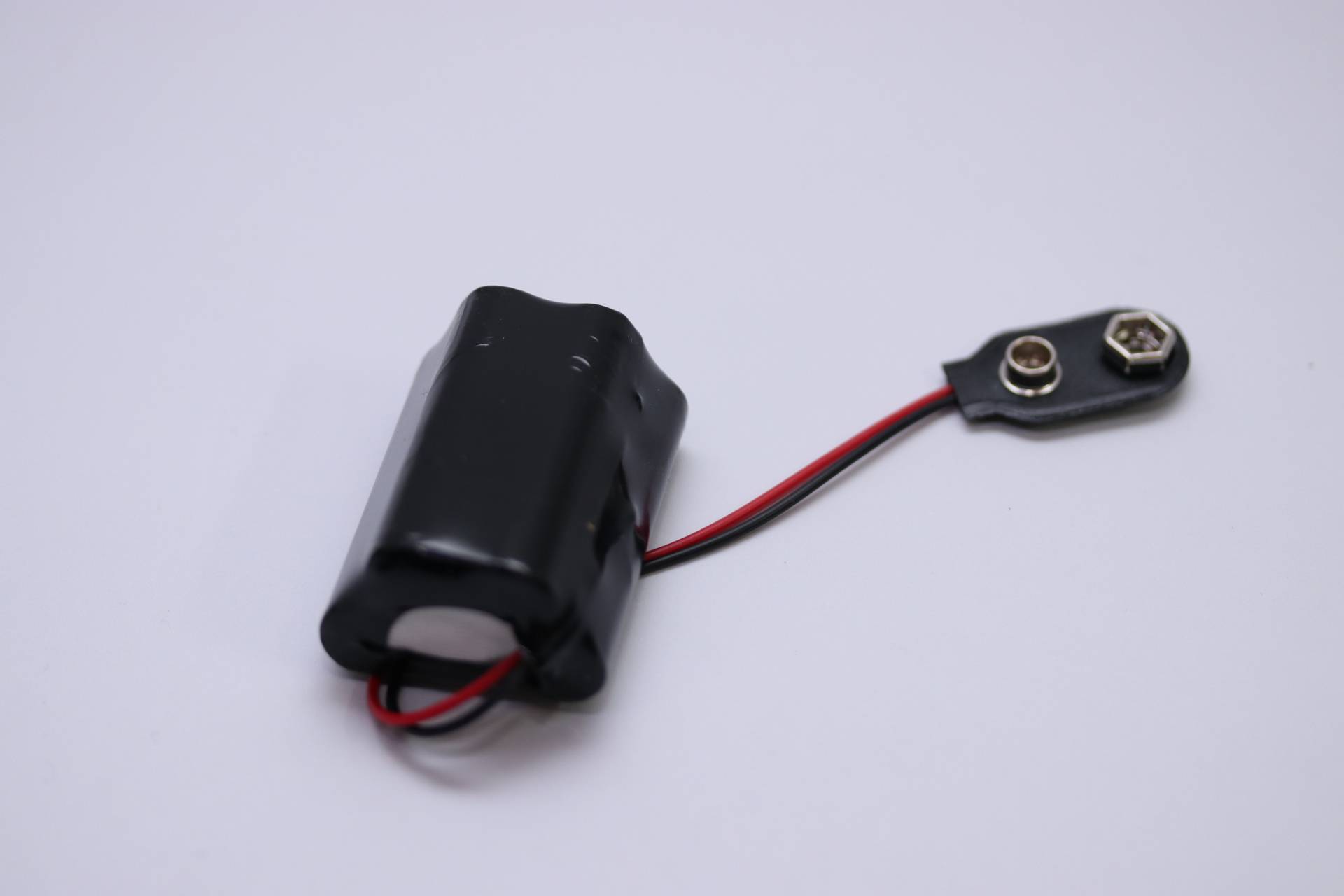 Eine schwarze zylindrische Batteriebox mit roten und schwarzen Kabeln, die an einen Batteriehalter angeschlossen ist.