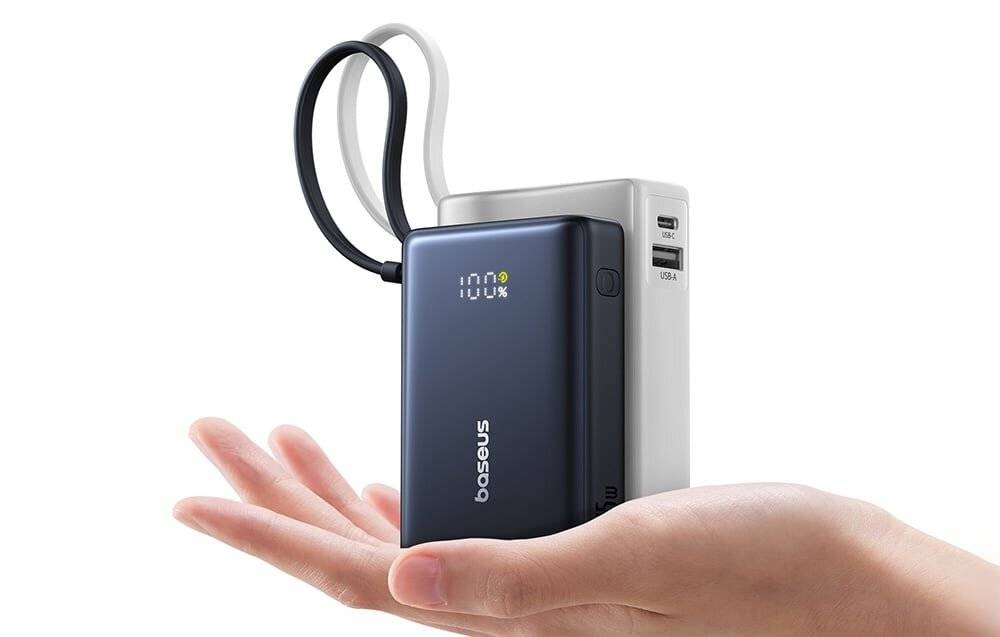 Eine Person hält eine kompakte tragbare Powerbank in Schwarz und Weiß mit drei Ladeanschlüssen. Sie zeigt einen digitalen Ladezustandsanzeige in Prozent an.