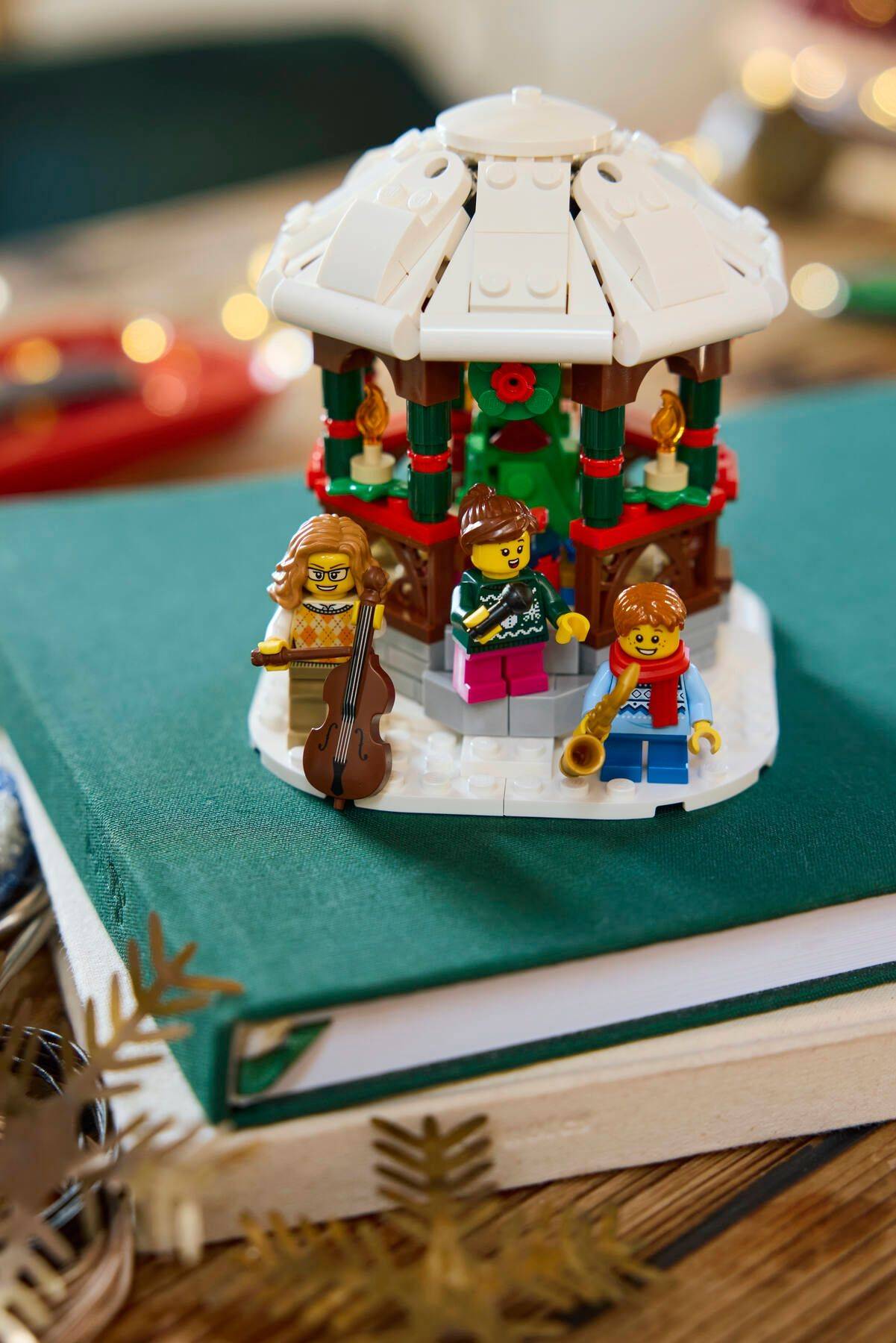 Eine LEGO-Szene mit Minifiguren, die Musikinstrumente in einem festlichen Pavillon spielen, aufgebaut auf einem Buch mit Weihnachtsmotiv.