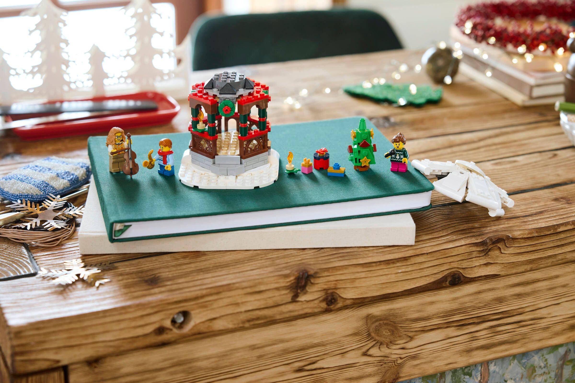 Eine festliche Lego-Szene auf einem Notizbuch zeigt einen Musikpavillon mit Kränzen, Figuren, die Musik spielen, und kleinen weihnachtlich gestalteten Dekorationen.