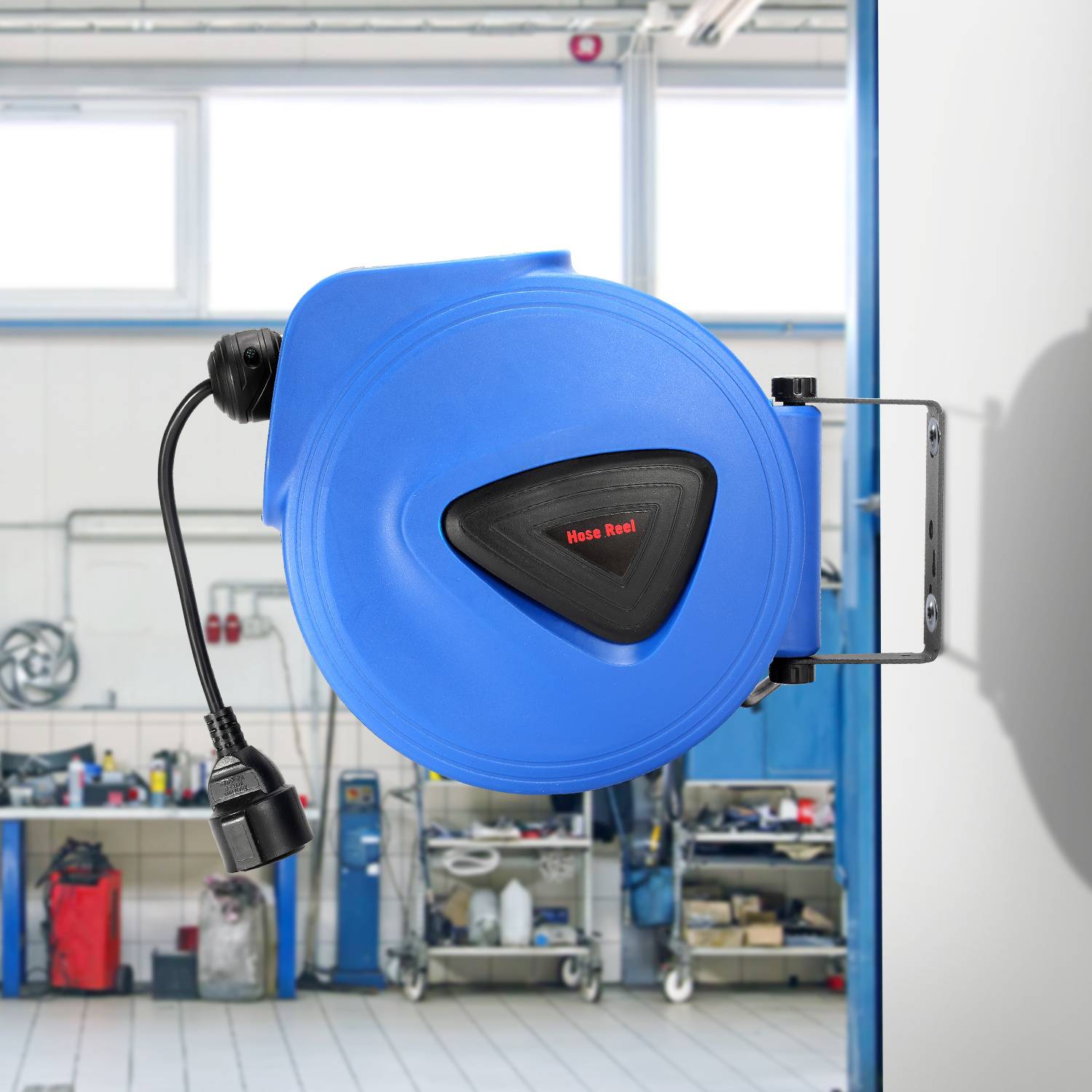 Eine blaue einziehbare Schlauchtrommel ist an einer Wand einer gut beleuchteten Werkstatt montiert, mit Werkzeugen und Ausrüstung im Hintergrund.