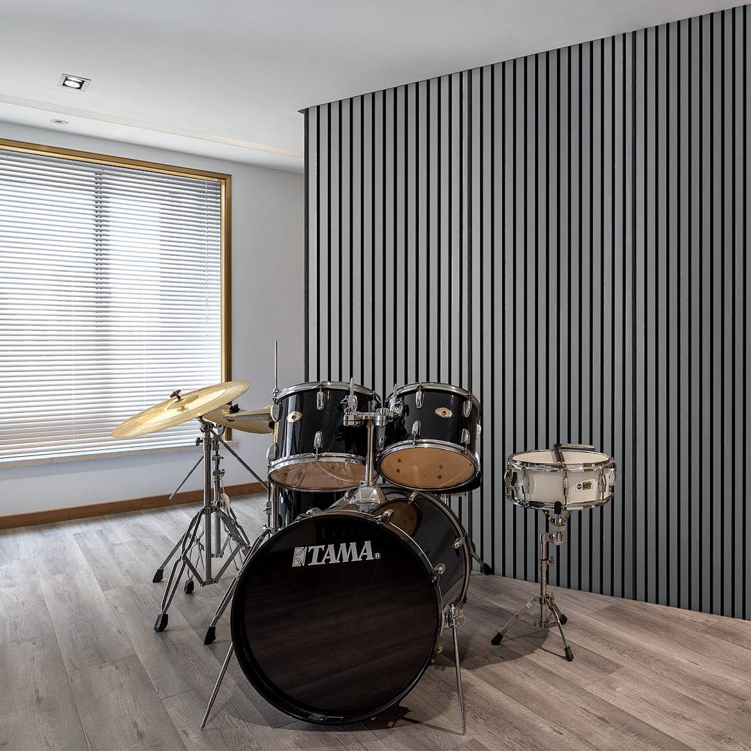 Ein Schlagzeug mit zwei Becken und einer Snare-Drum ist in einem modernen Raum mit gestreifter Tapete und einem Fenster mit Jalousien aufgestellt.