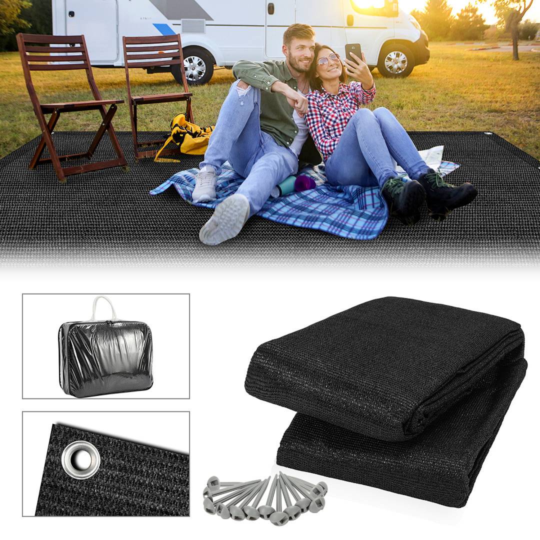 Ein Paar sitzt auf einer Picknickdecke mit einem Campingwagen im Hintergrund. Darunter sind eine zusammengelegte Matte, Heringe und eine Tragetasche ausgelegt.