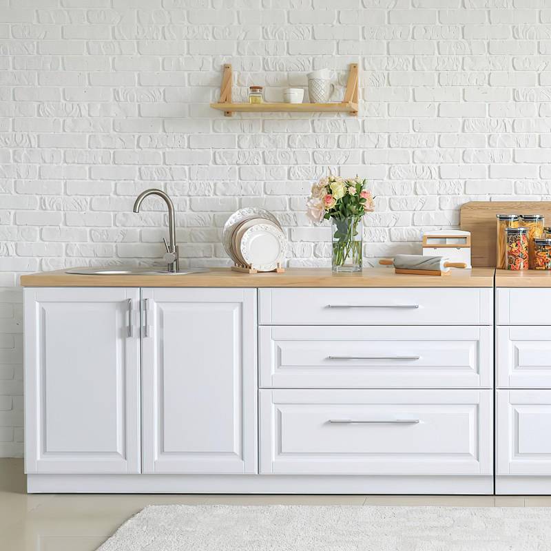 Moderne Küche mit weißer Ziegelwand, Holzarbeitsplatte und Regalen. Ausgestattet mit Spüle, Behältern, Küchenutensilien und einer Blumenvase.