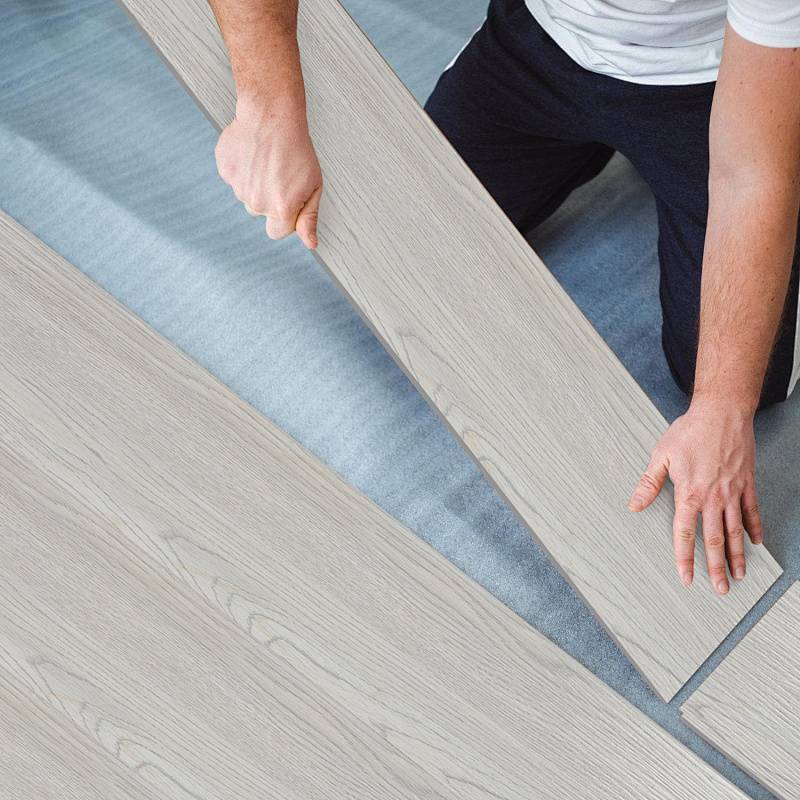 Eine Person verlegt Holzfußbodenplatten und richtet sie präzise aus. Die Platten haben eine helle Holzmaserungstextur.