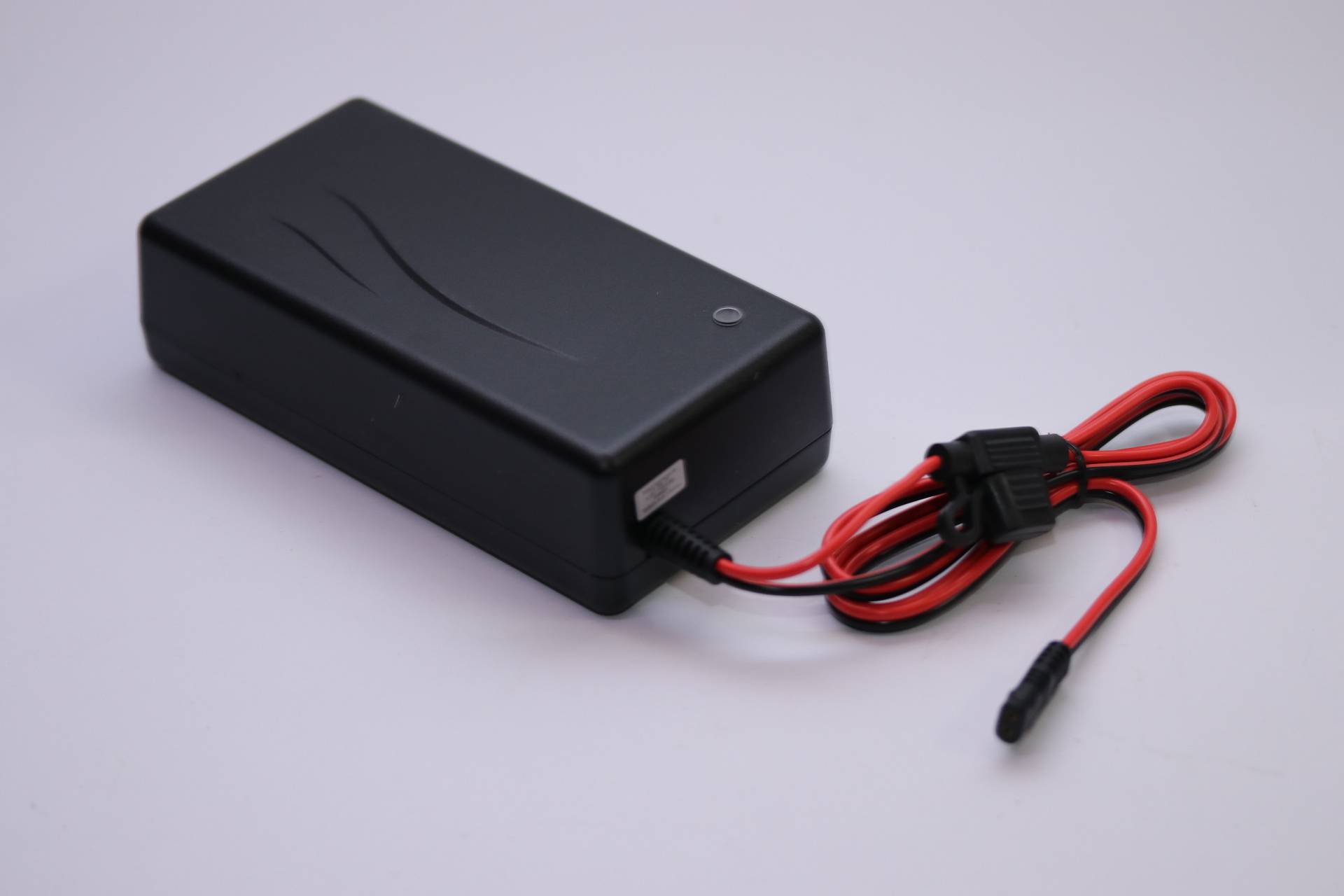 Ein schwarzes Netzteil mit einem roten Kabel, auf einer weißen Oberfläche platziert.