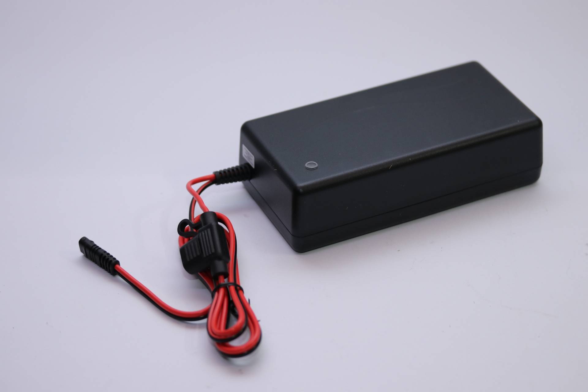 Ein schwarzes Netzteil mit einem rot-schwarzen Kabel, das darum gewickelt ist, auf einer flachen, hellgrauen Oberfläche liegend.