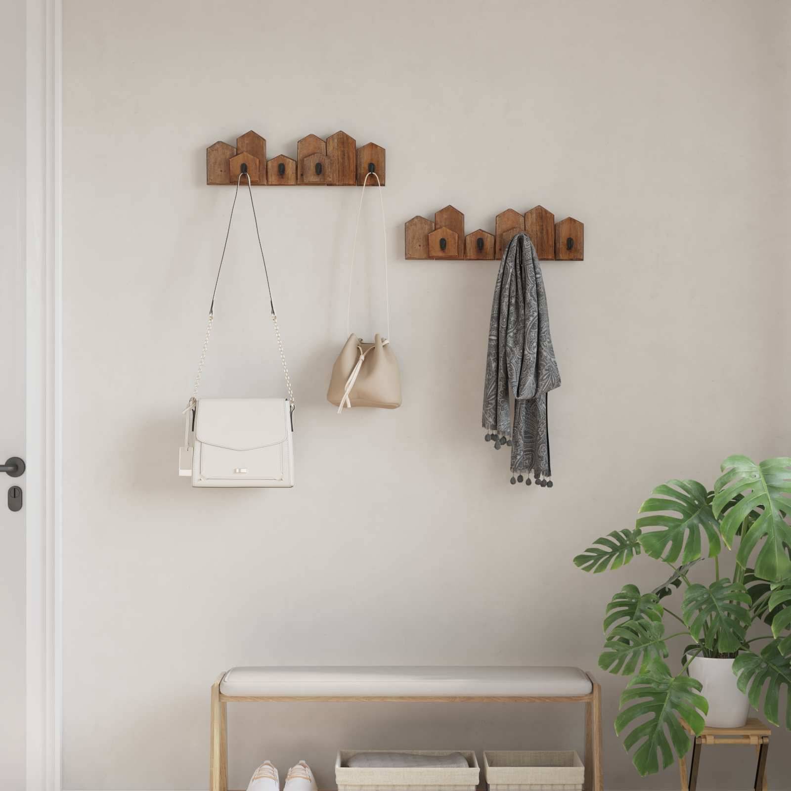 Eine minimalistische Diele zeigt zwei an der Wand montierte Holz-Kleiderhaken, an denen eine Handtasche, ein Hut und ein Schal hängen. Unter den Haken stehen eine Bank und eine Pflanze.