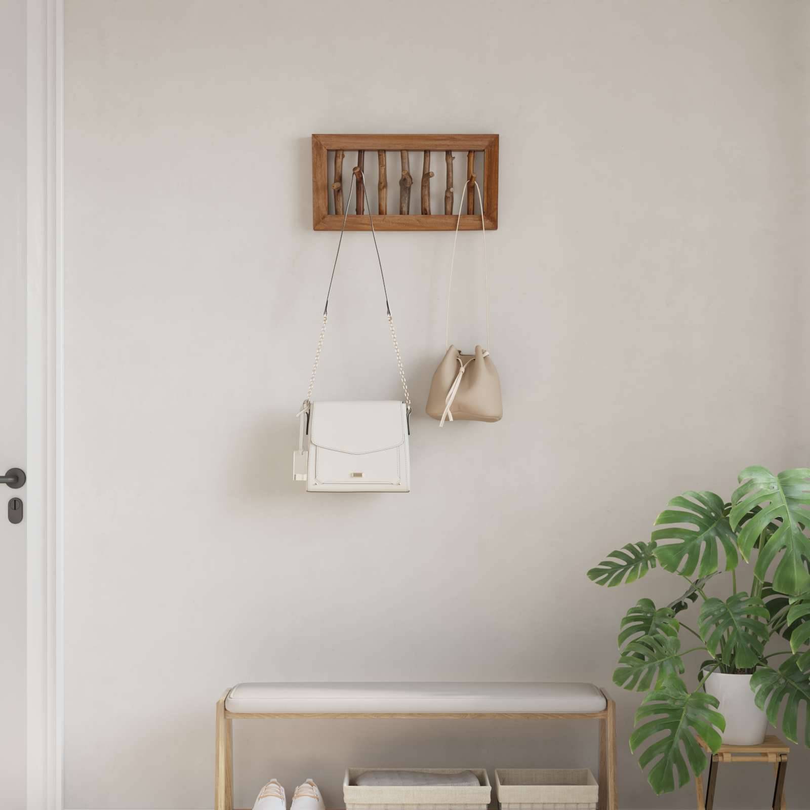 Eine minimalistische Diele zeigt einen an der Wand montierten Holz-Garderobenständer mit hängenden Taschen, eine Bank mit Stauraum darunter und eine Zimmerpflanze daneben.